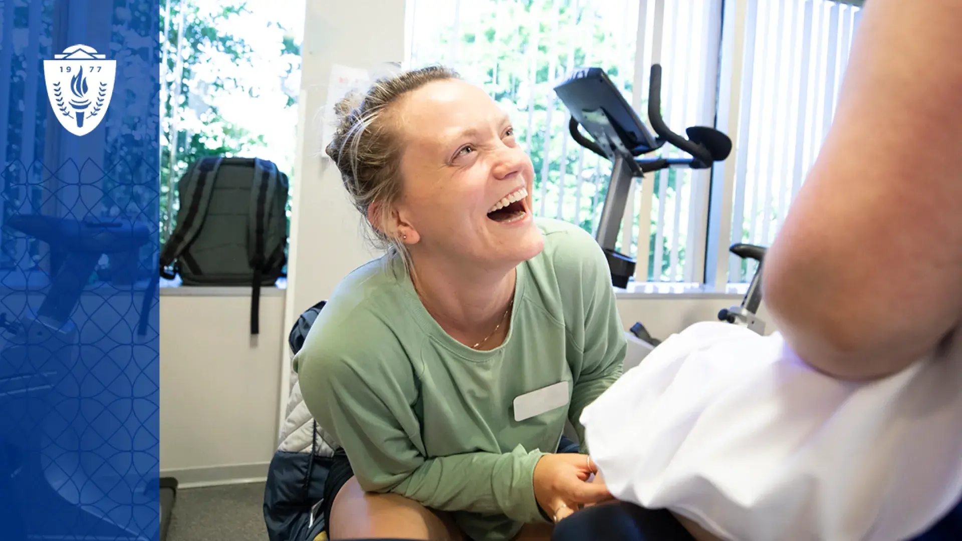 woman smiles broadly up at a person on a treatment table while she helps them move their leg