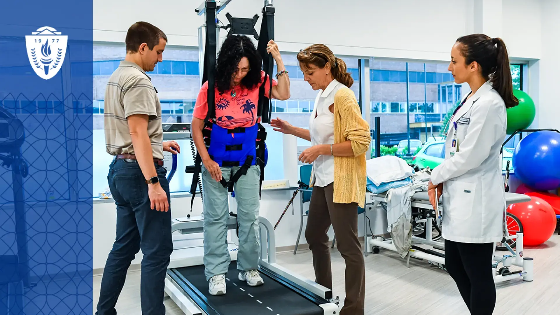 three people stand around a woman in a harness suspended over a treadmill in a gym