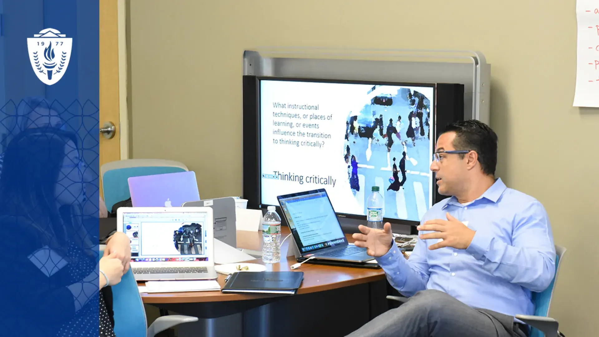 man gestures in a way that indicates teaching at a table with other adults