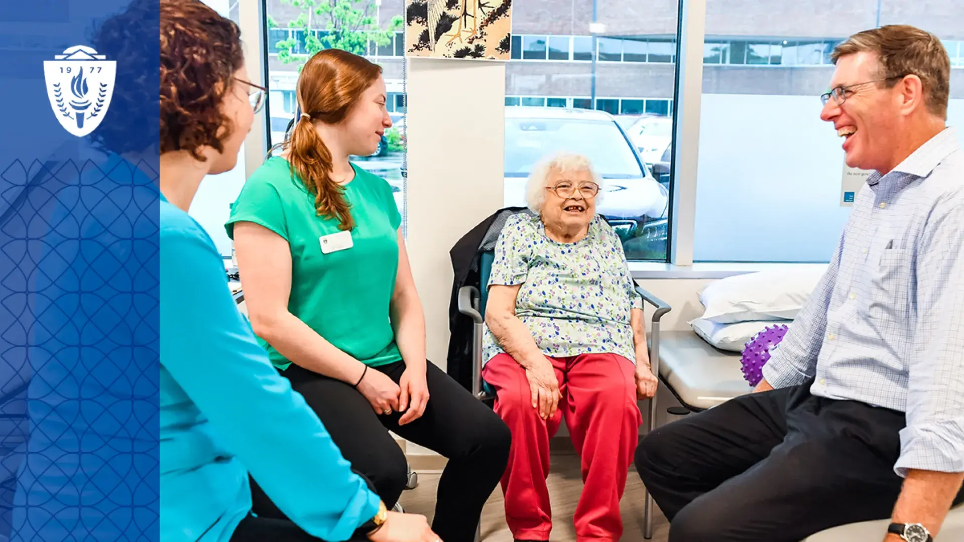 group of people sit around an older woman in a PT gym
