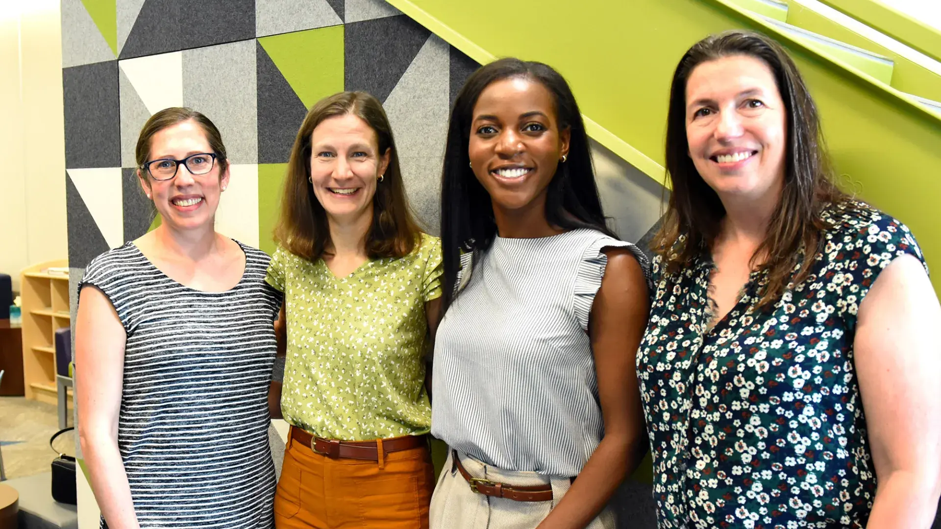 four women stand in front of a green staircase