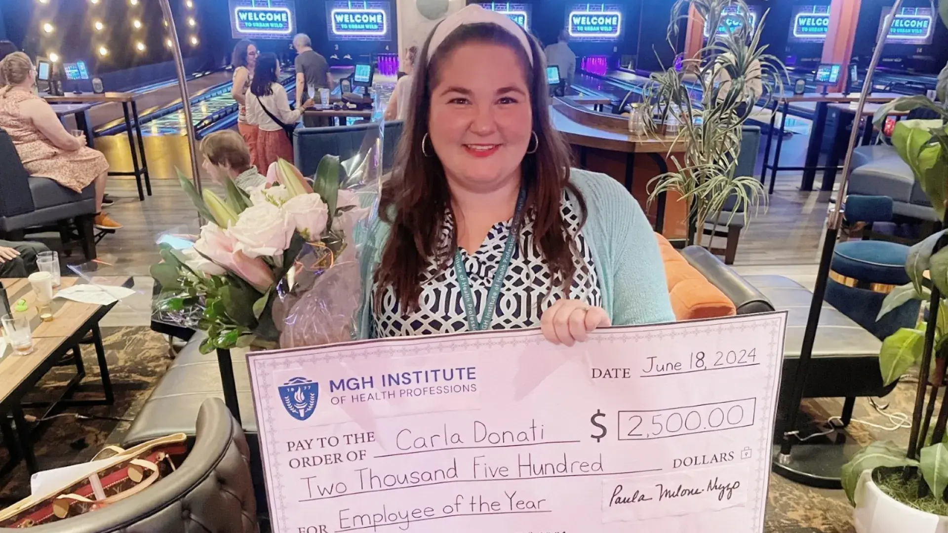 A woman poses holding flowers and a large check
