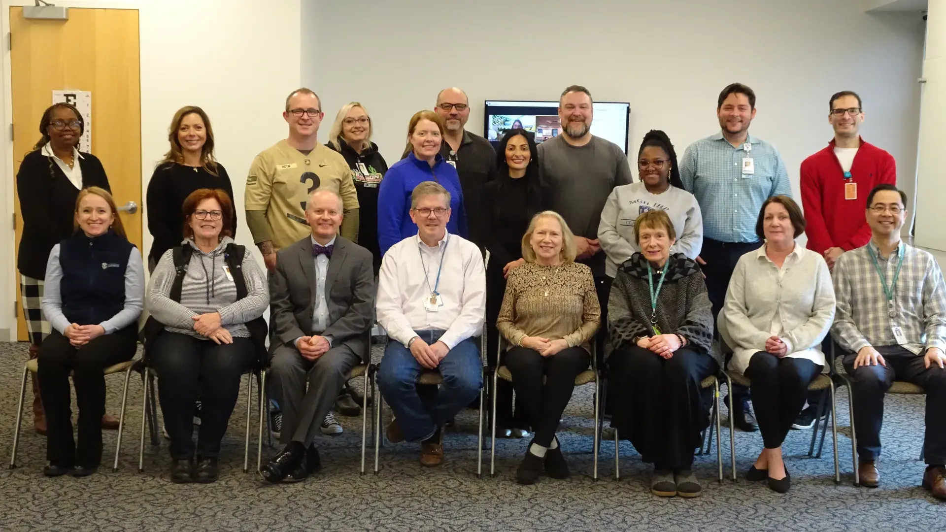 A group of people posing for a photo with eight people sitting in the front row and 11 standing behind them