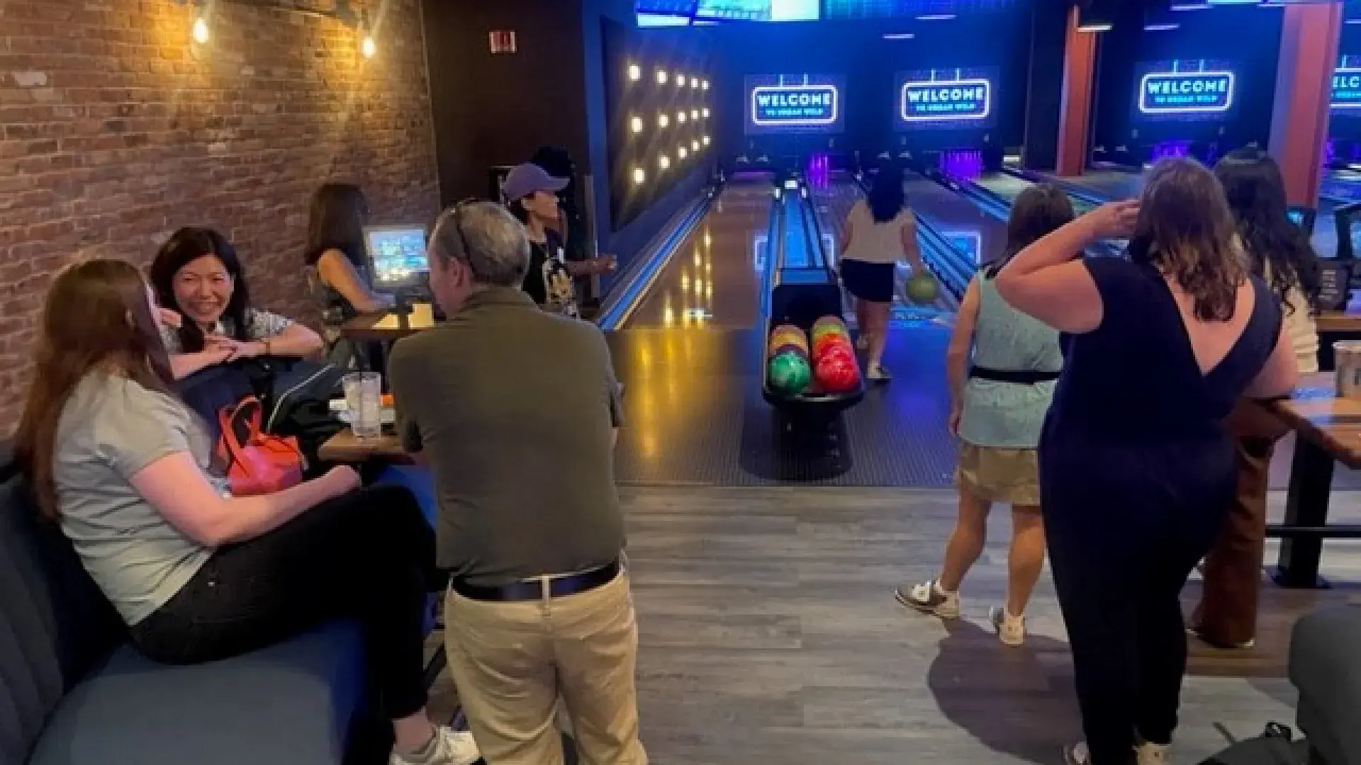 A group of people socializing and three others watching someone bowl