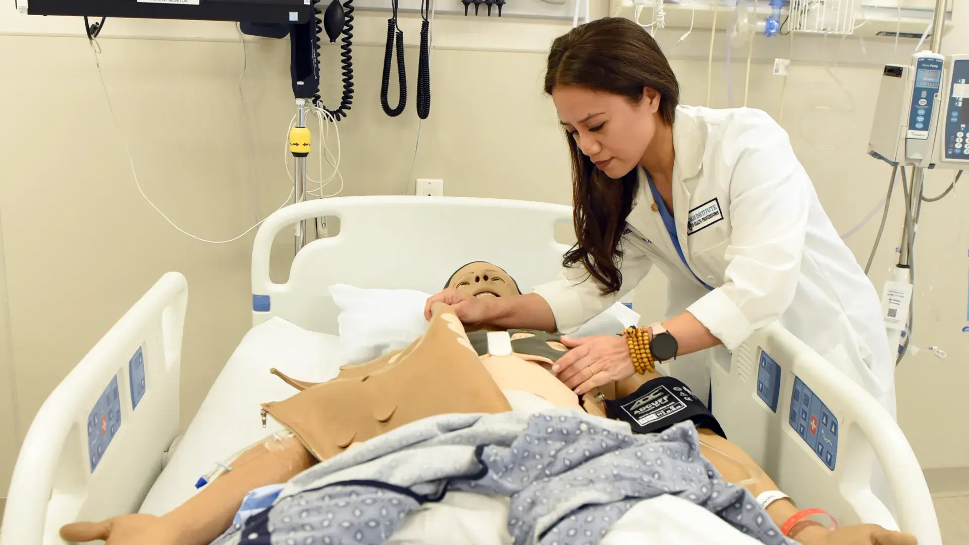 a woman in a lab coat leans over a manikin in a hospital bed