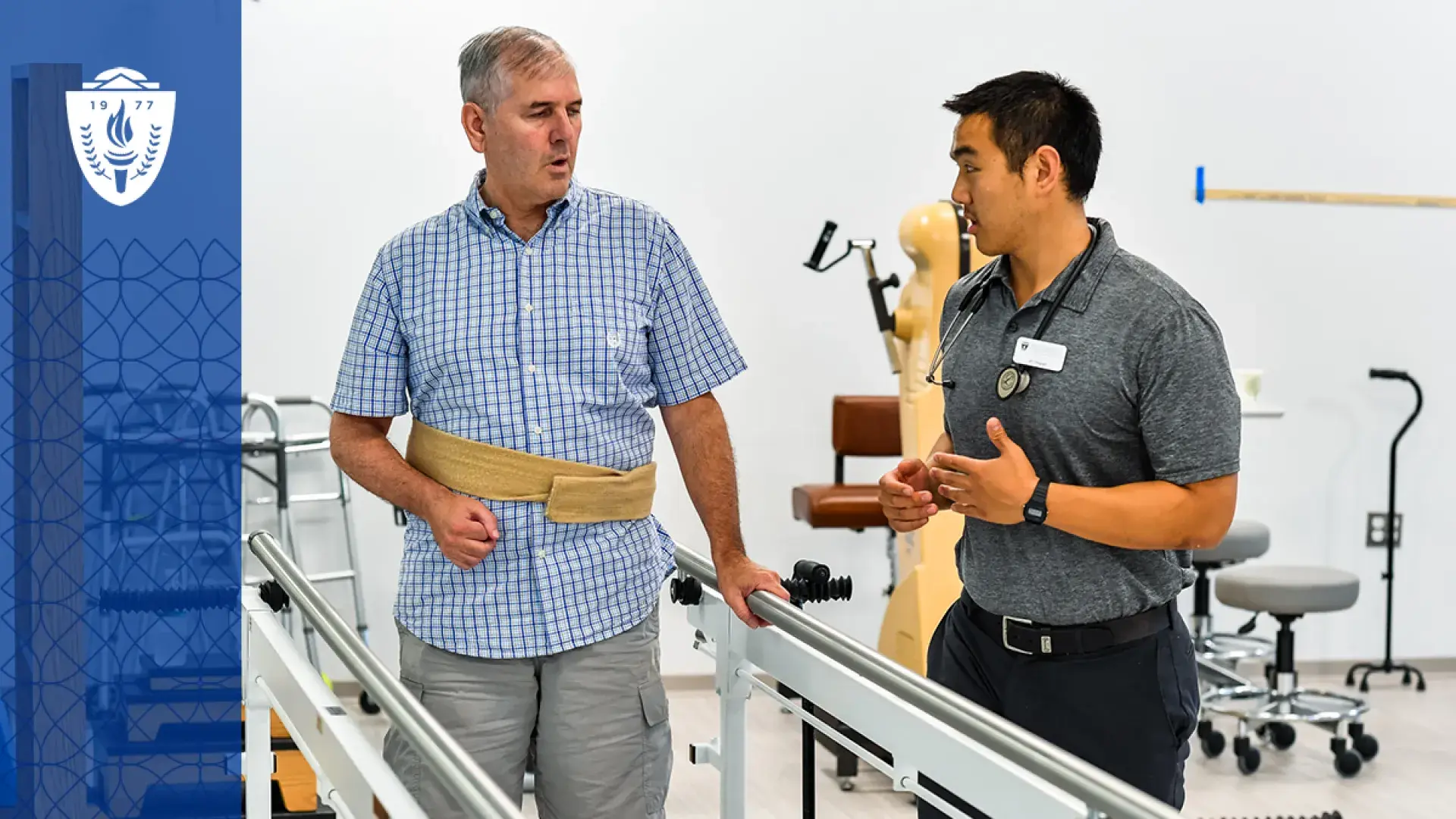 older man with a strap around his waist stands between parallel bars while a young man explains something to him