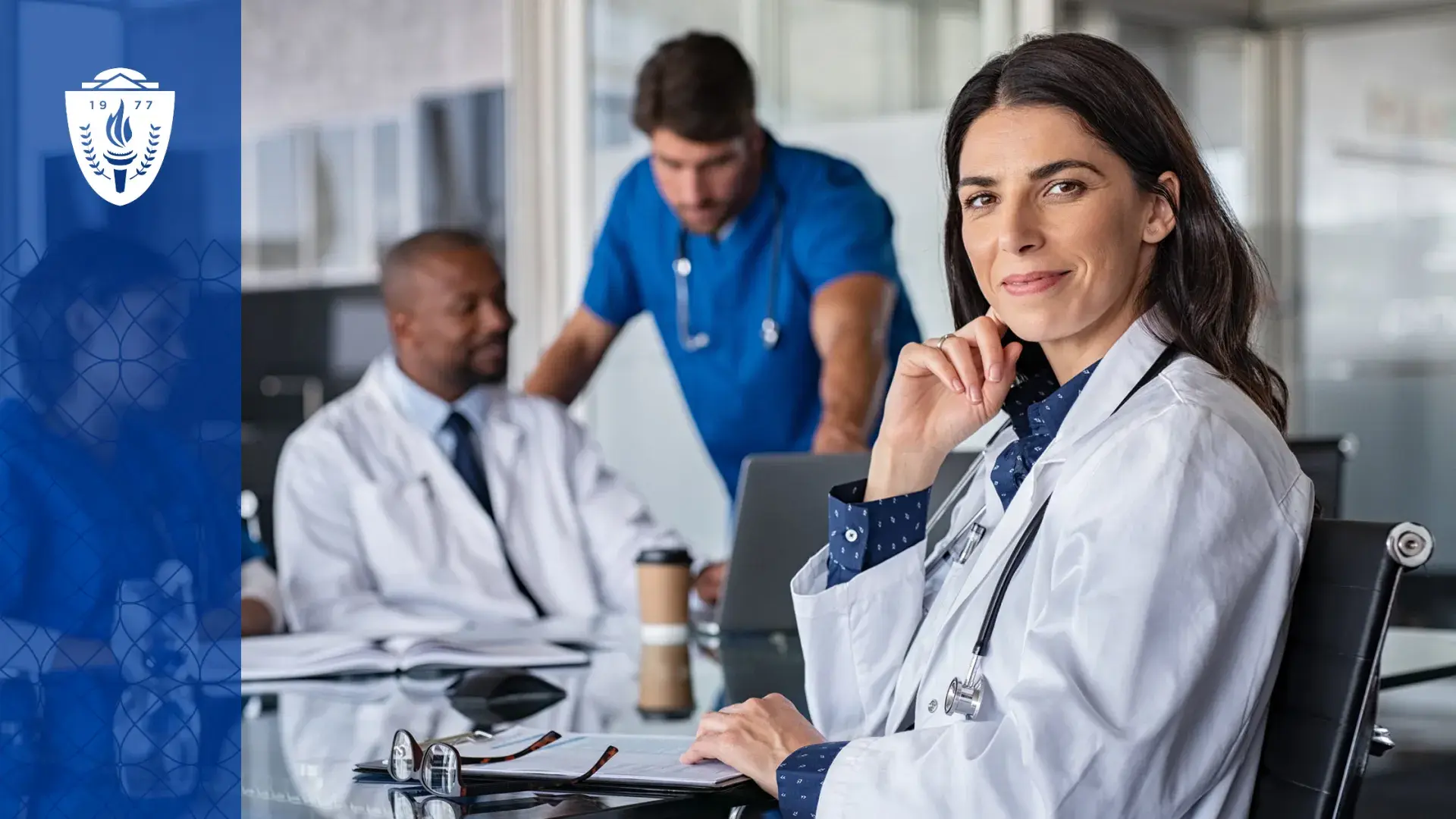 woman in lab coat sits at a conference table and knowingly smiles at the camera