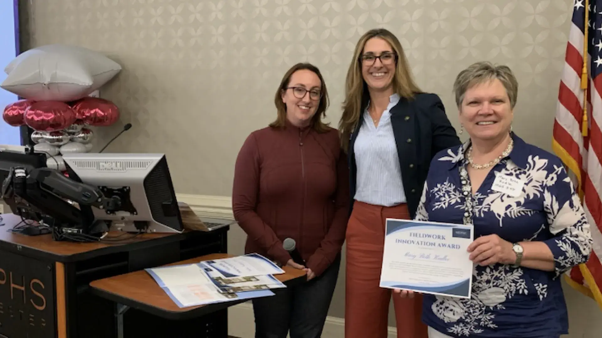Three women smile while holding a certificate.