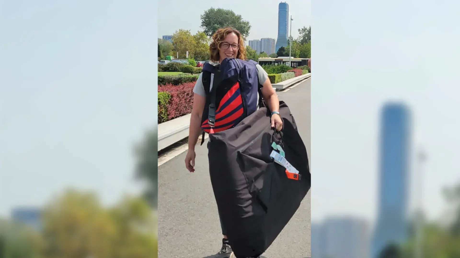 woman stands on a paved path with buildings and flowers in the background