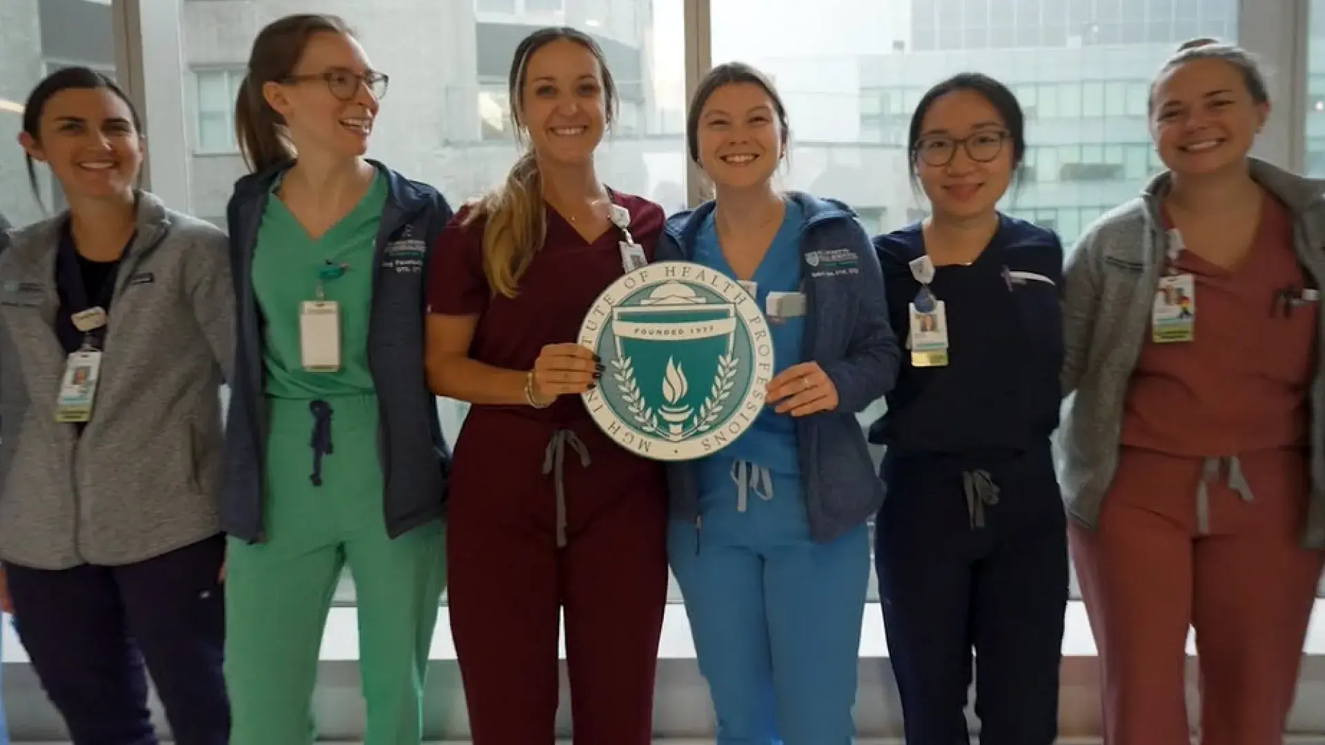 group of people in scrubs standing with the IHP logo which is a shield and laurel leaves