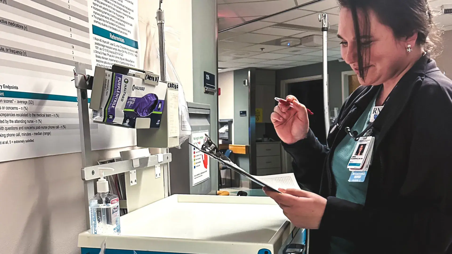 a woman in scrubs checks a chart in a hospital hallway