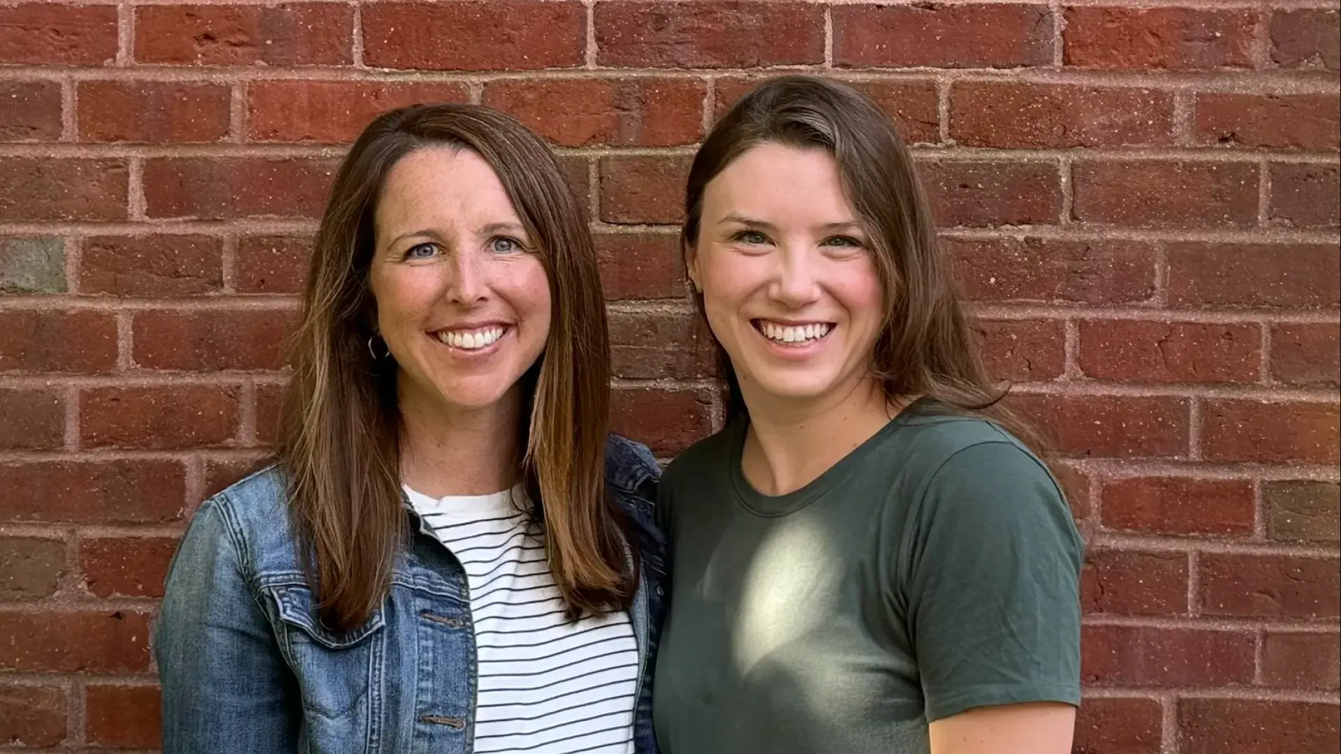 two women stand in front of a brick wall