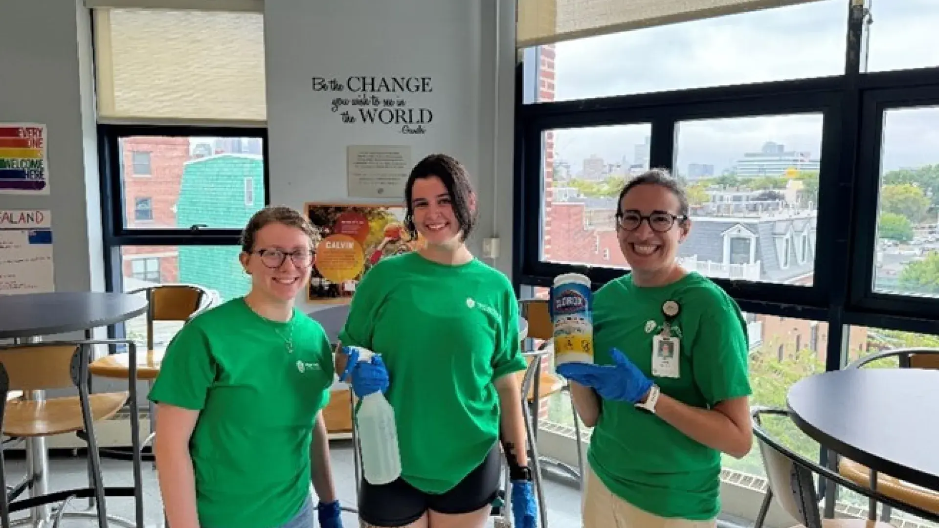 Three women pose holding cleaning items