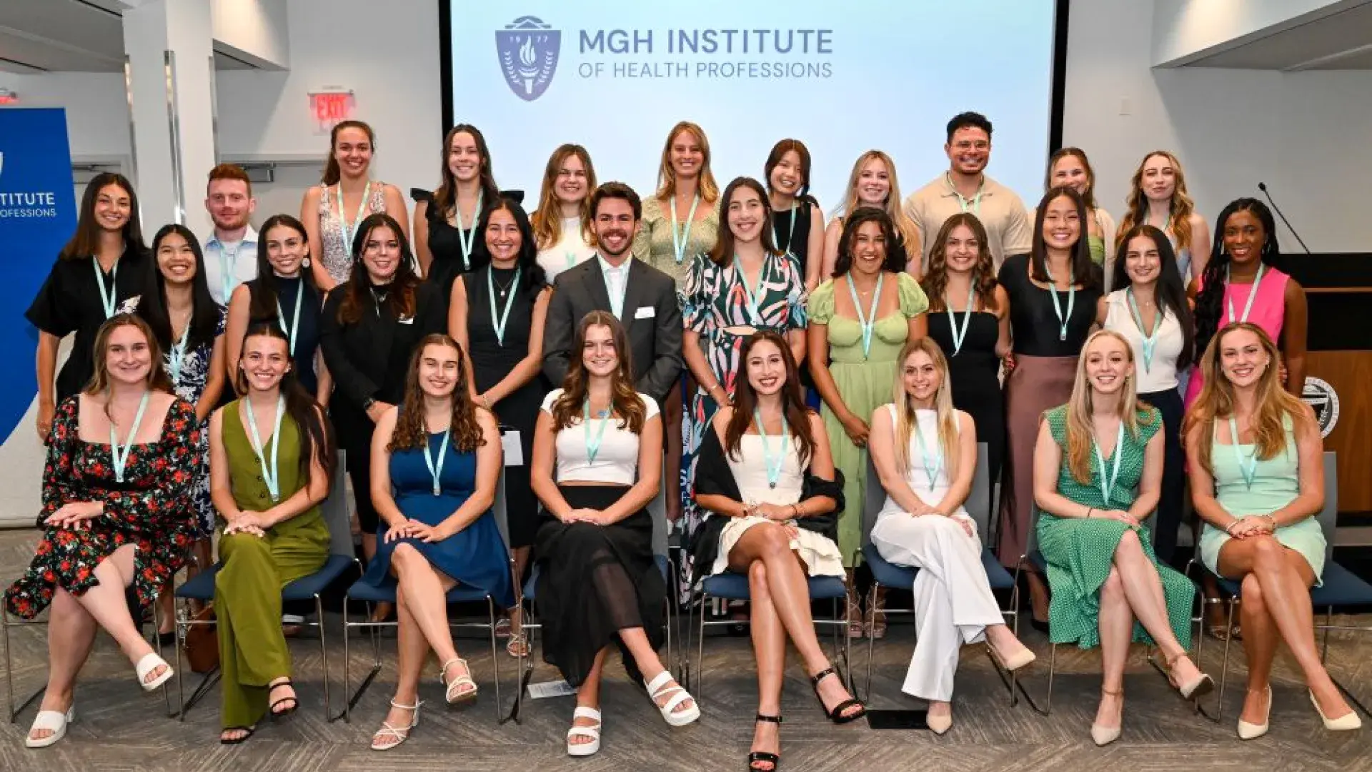 A group stands in three rows in front of a backdrop that says MGH Institute