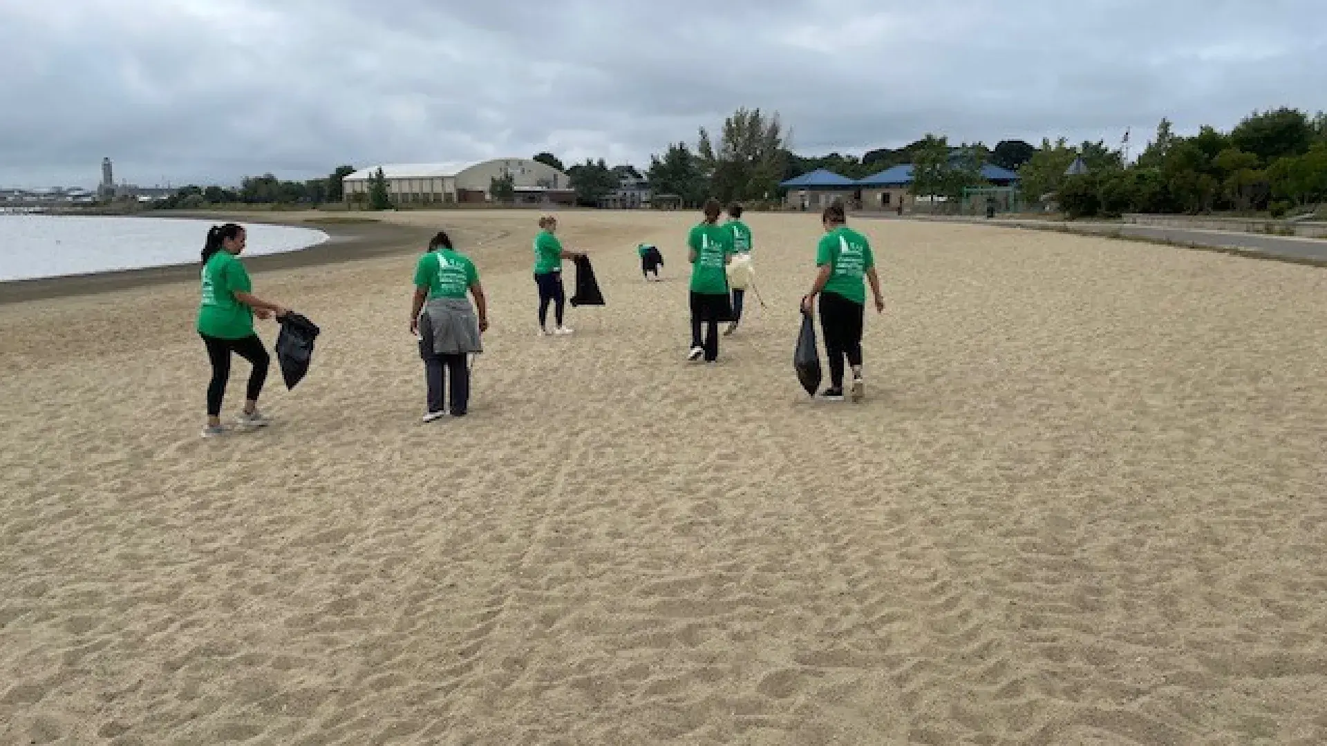 A group of people walking away from the camera and picking up trash on the beach