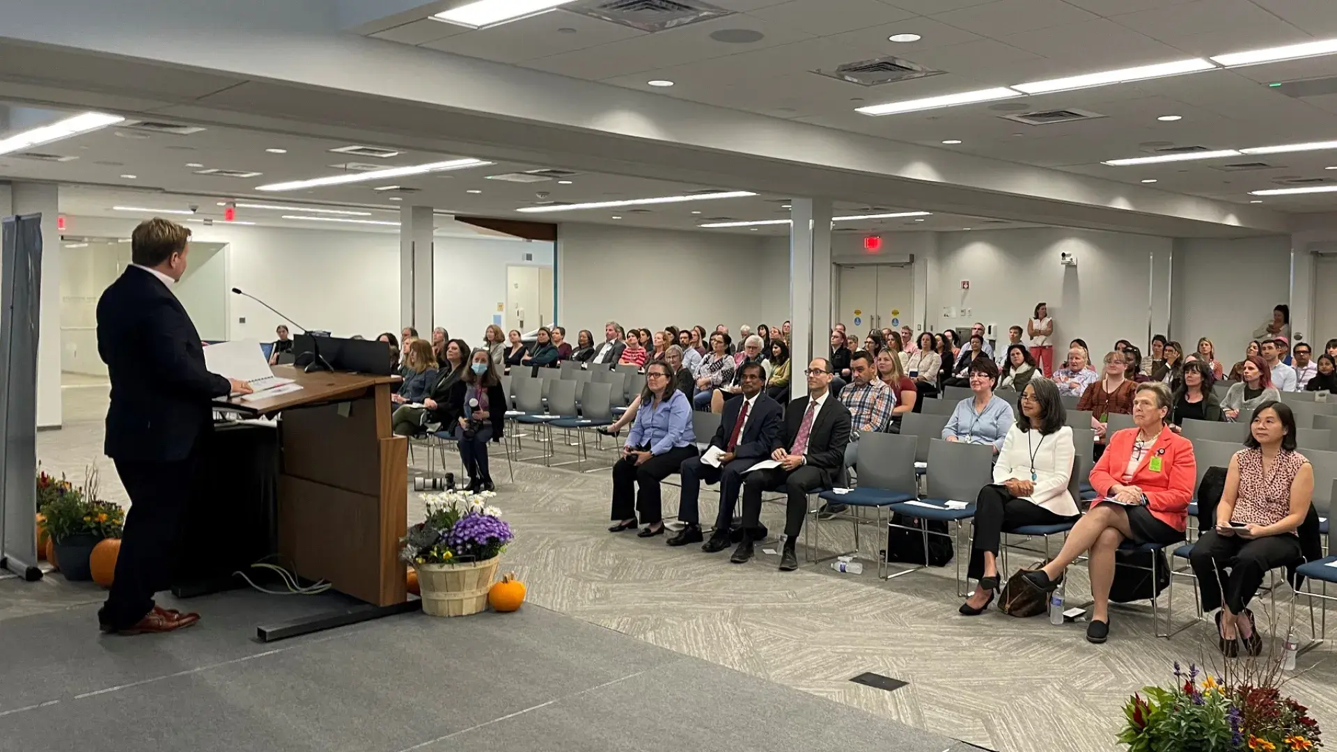 a large room with people seated listening to a man at a podium
