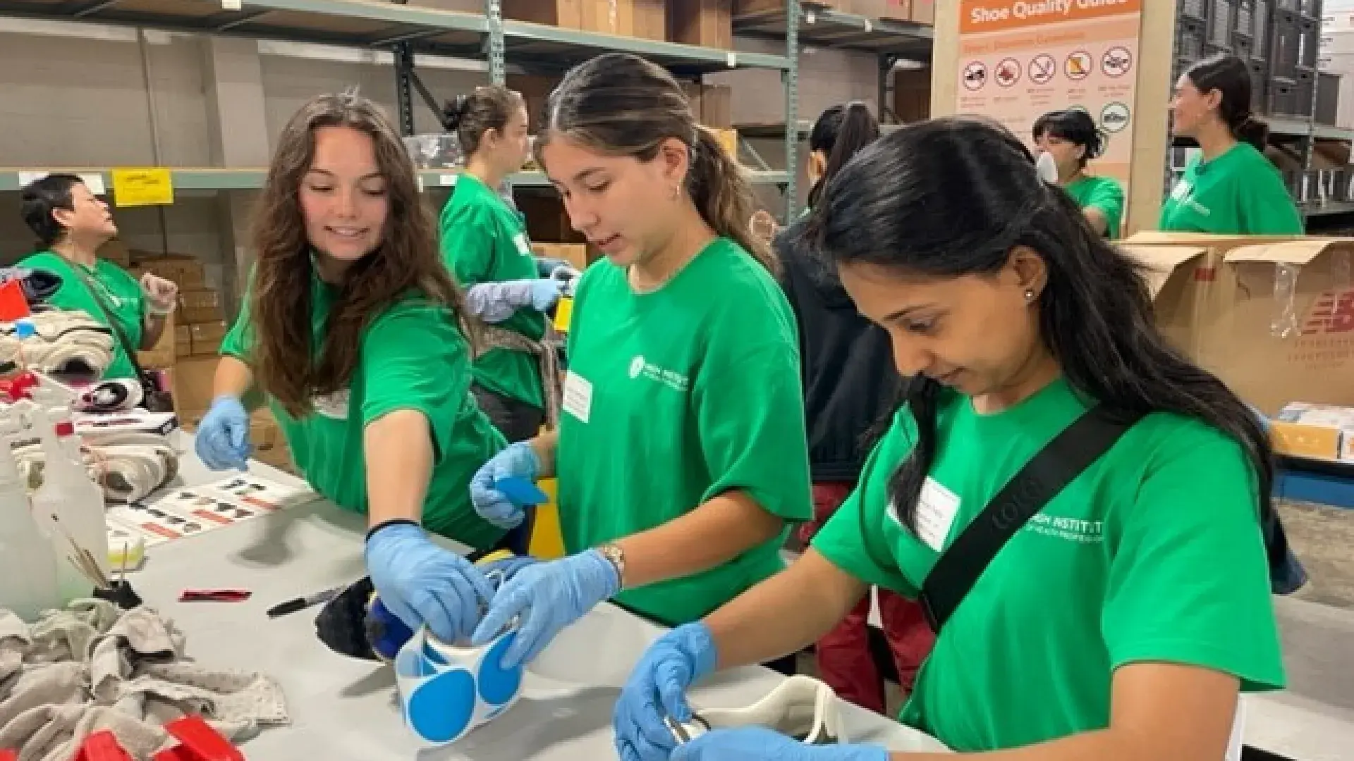 Three women stand at a table with shoes and stickers in front of them