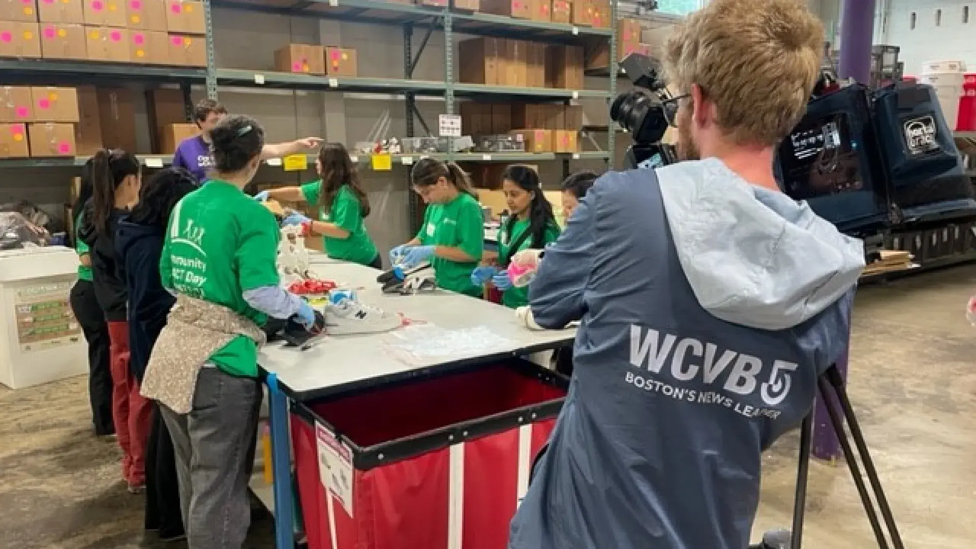 A videographer films a table with women around it who are working on sorting shoes