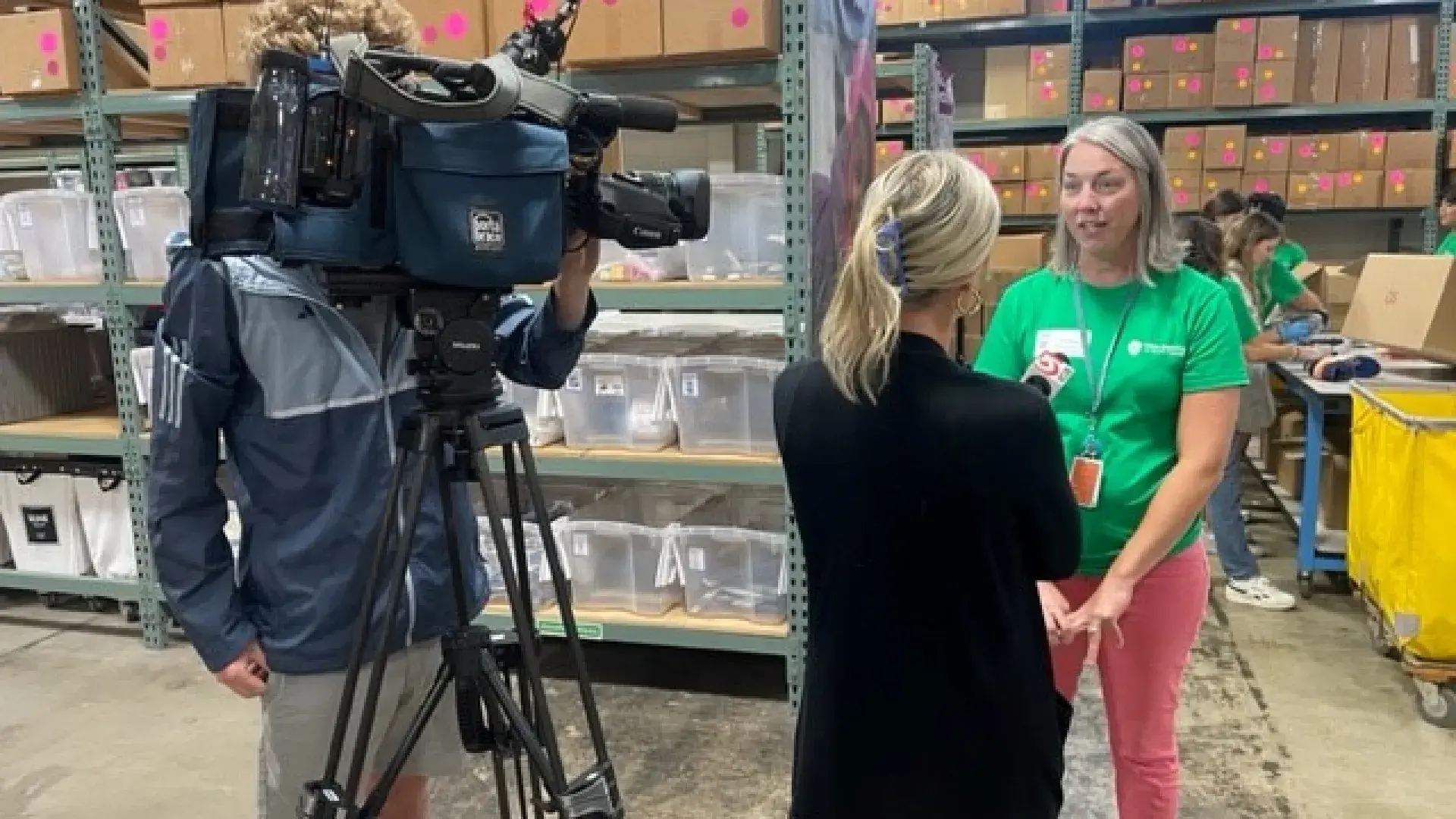 A woman holds a microphone toward another woman while a man with a video camera films them