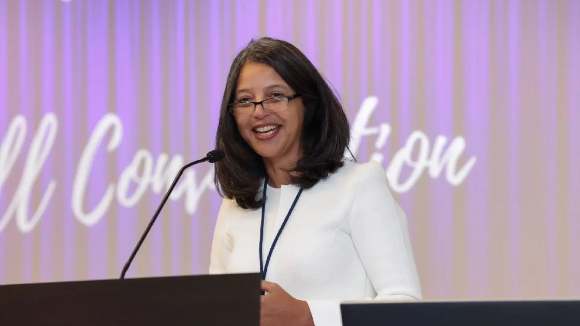A woman in a white top stands behind a podium with a microphone