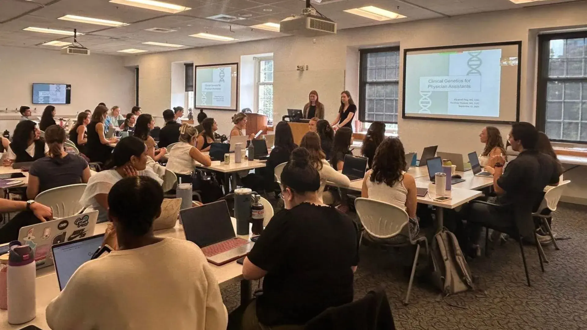 two people teaching in front of classroom of people