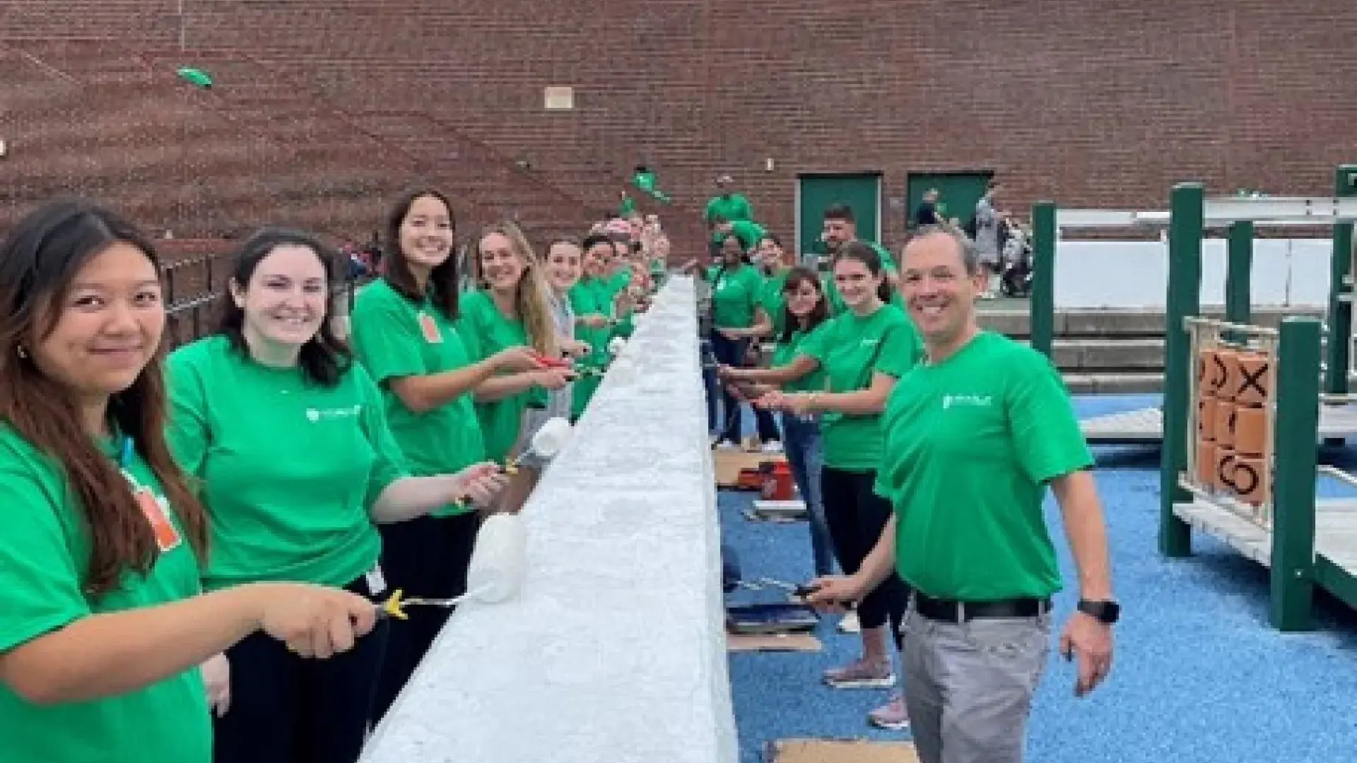 People line both sides of an outdoor wall with paint brushes