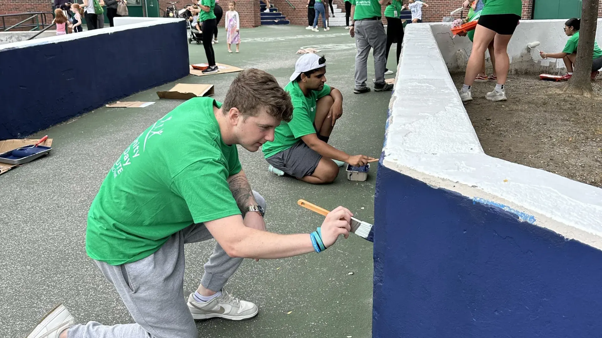 Two men paint a half wall while a woman further back paints the other side