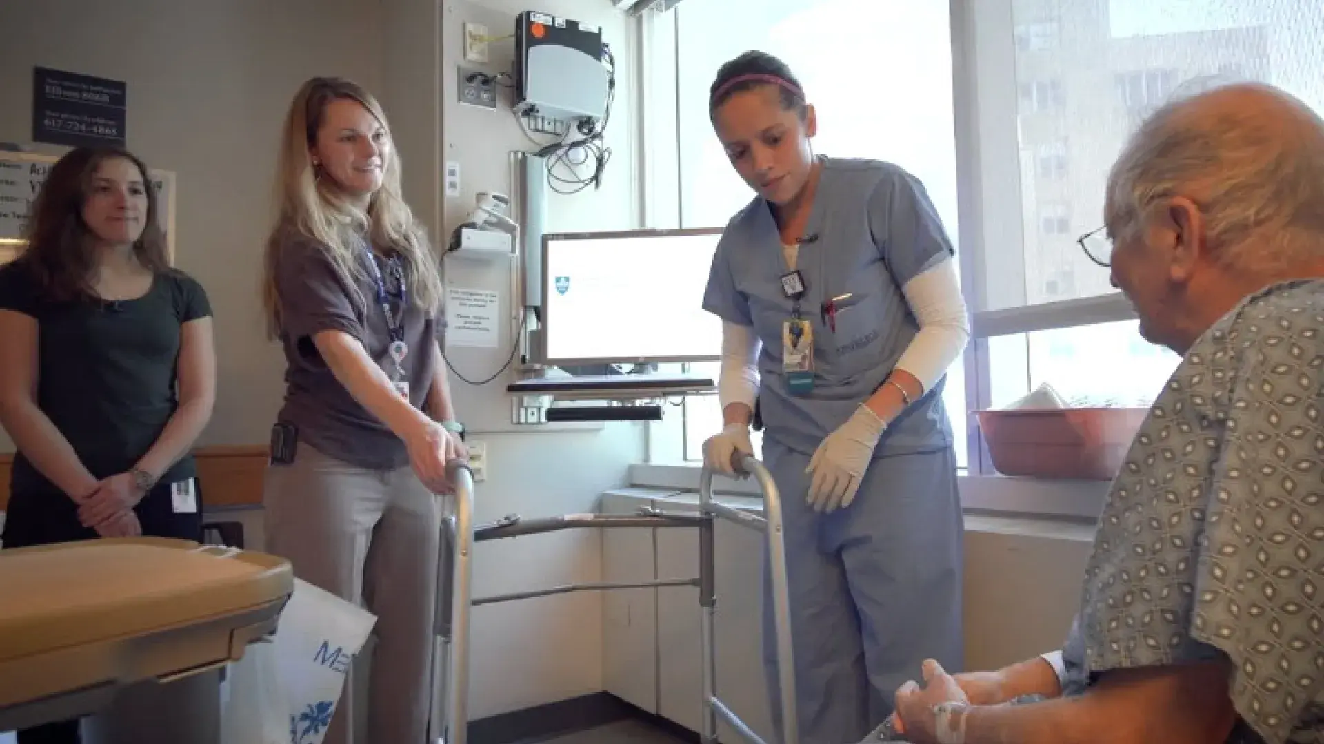 a woman in scrubs shows a walker to an old gentleman while two women in plain clothes look on