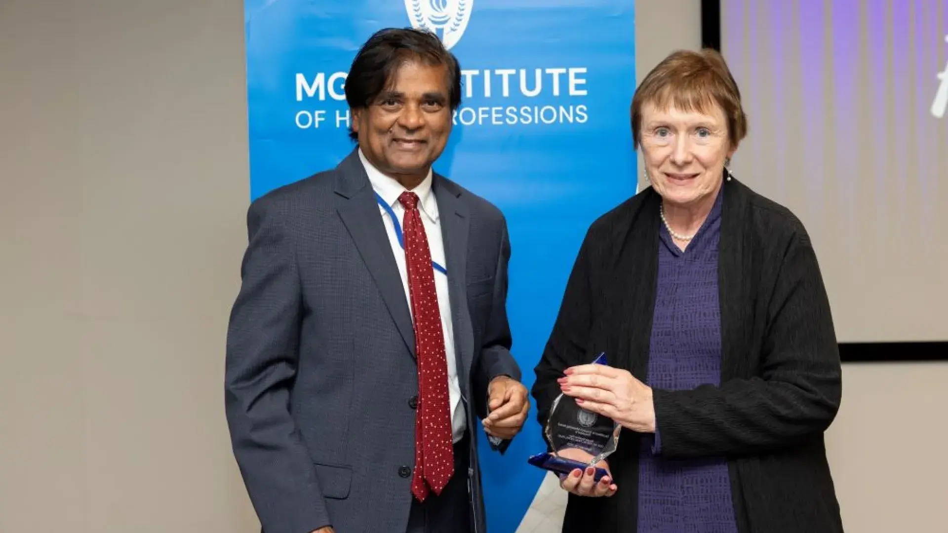 man and woman stand in front of MGH banner with award