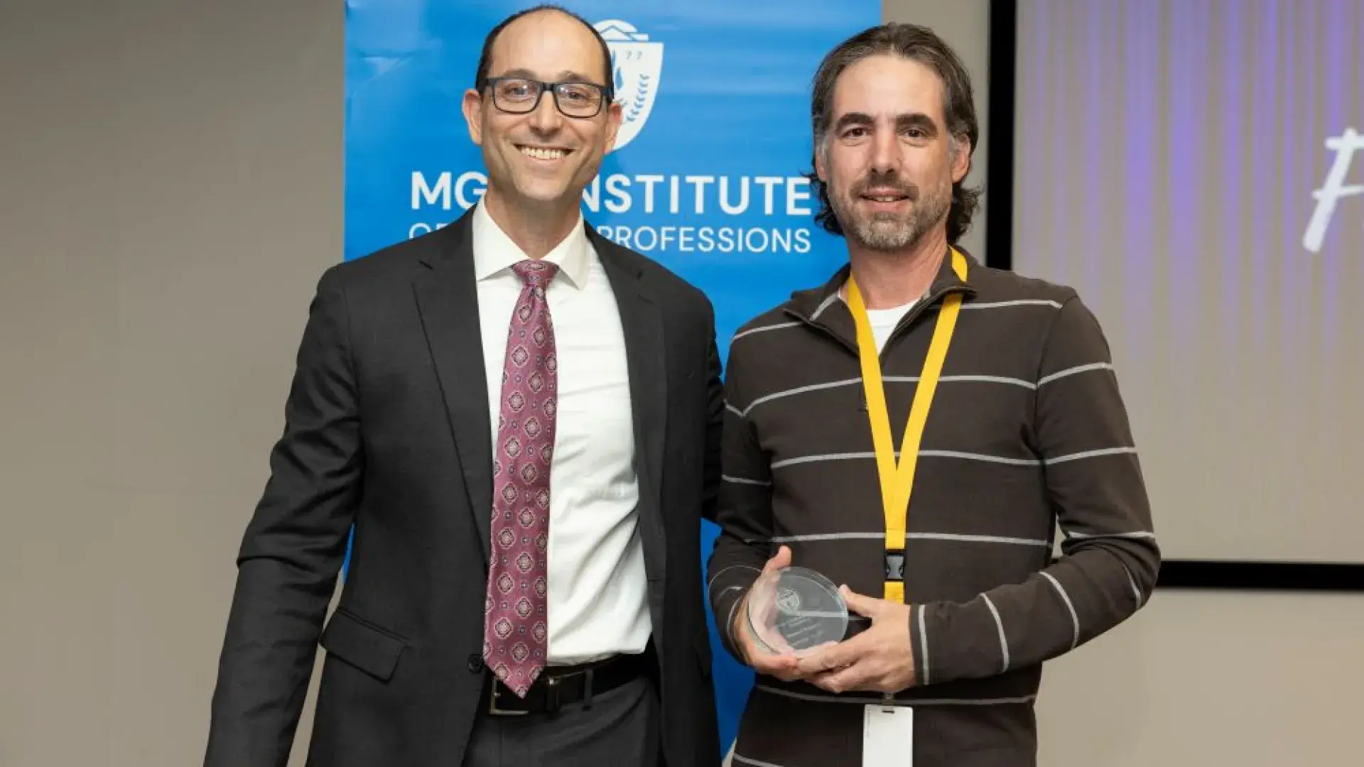 two men stand in front of MGH banner with award