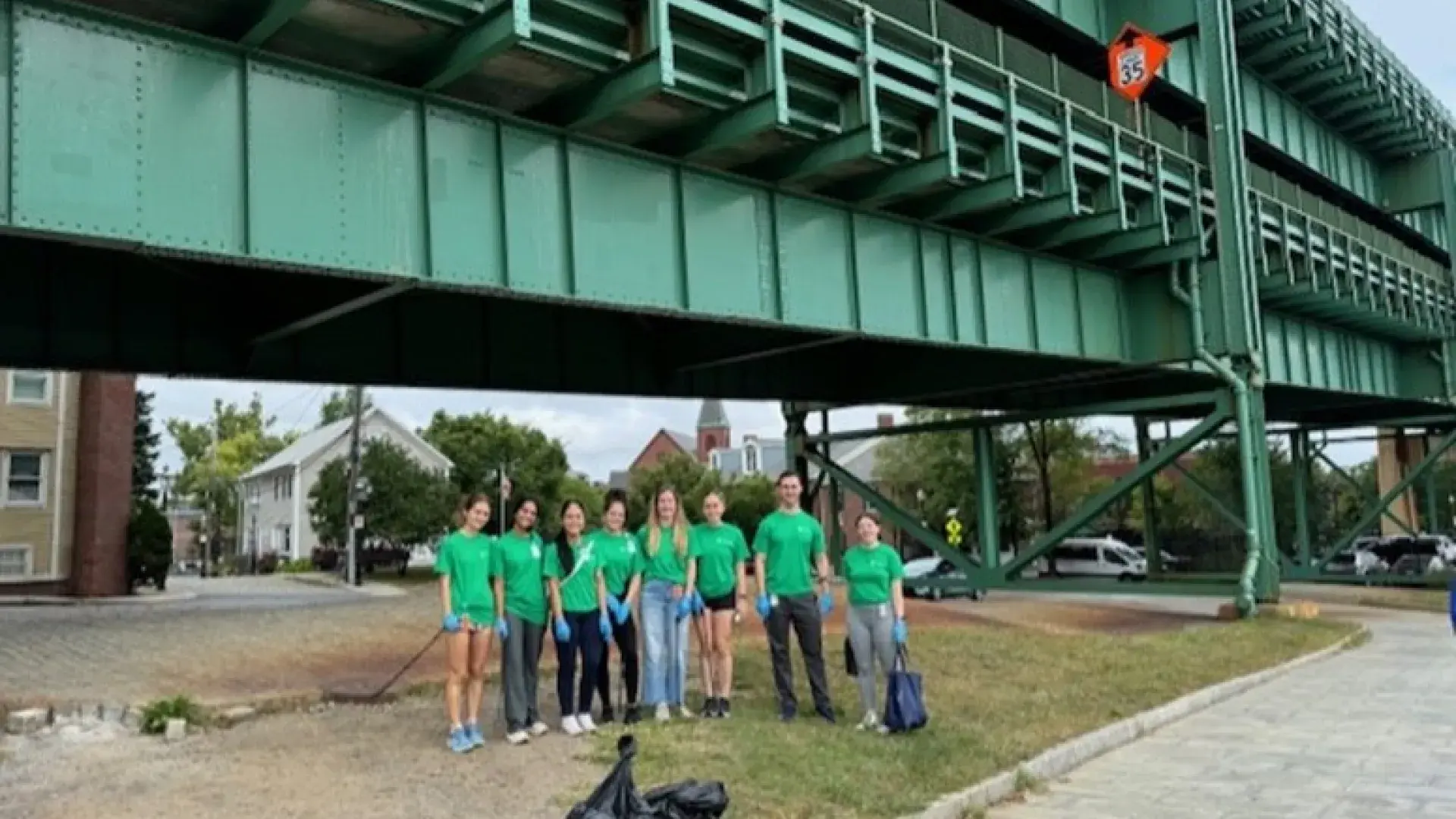 Eight people pose under a bridge with trash bags
