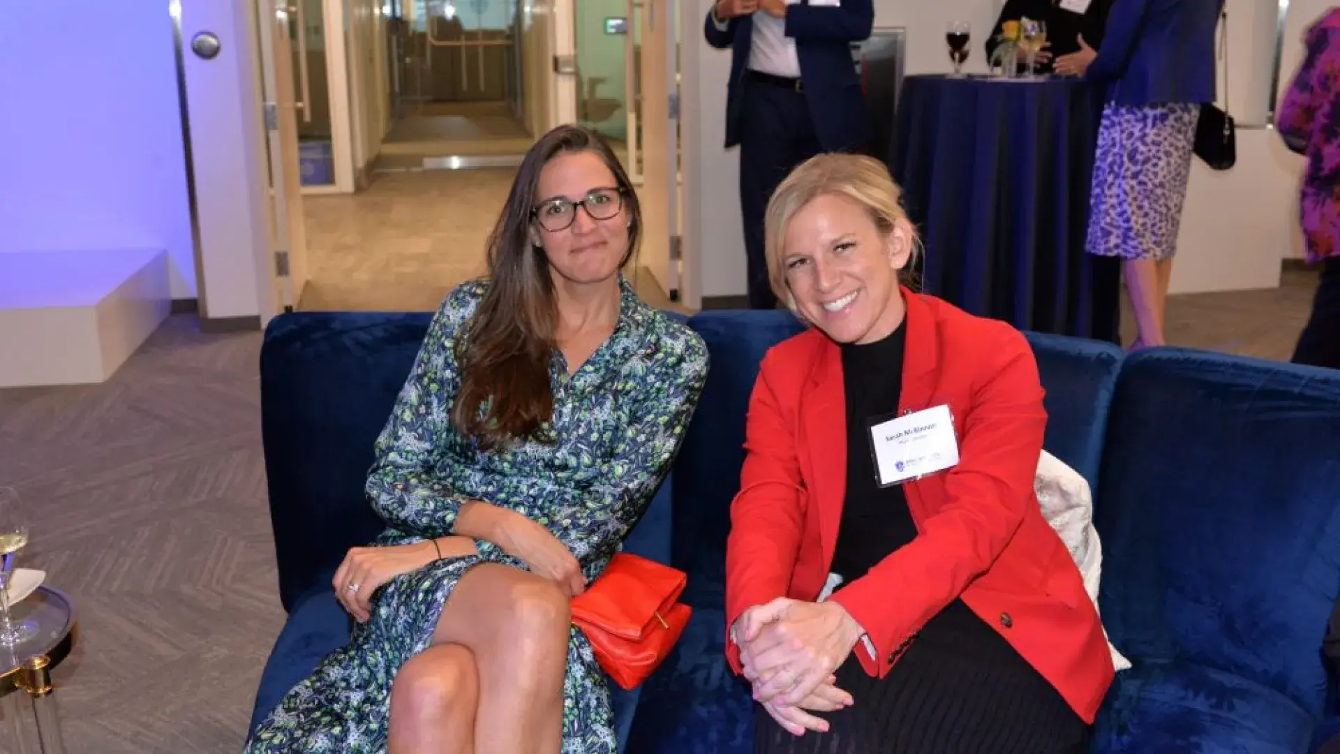 Two attendees seated on a blue sofa at the MGH Institute of Health Professions networking event, smiling and engaging with the camera.