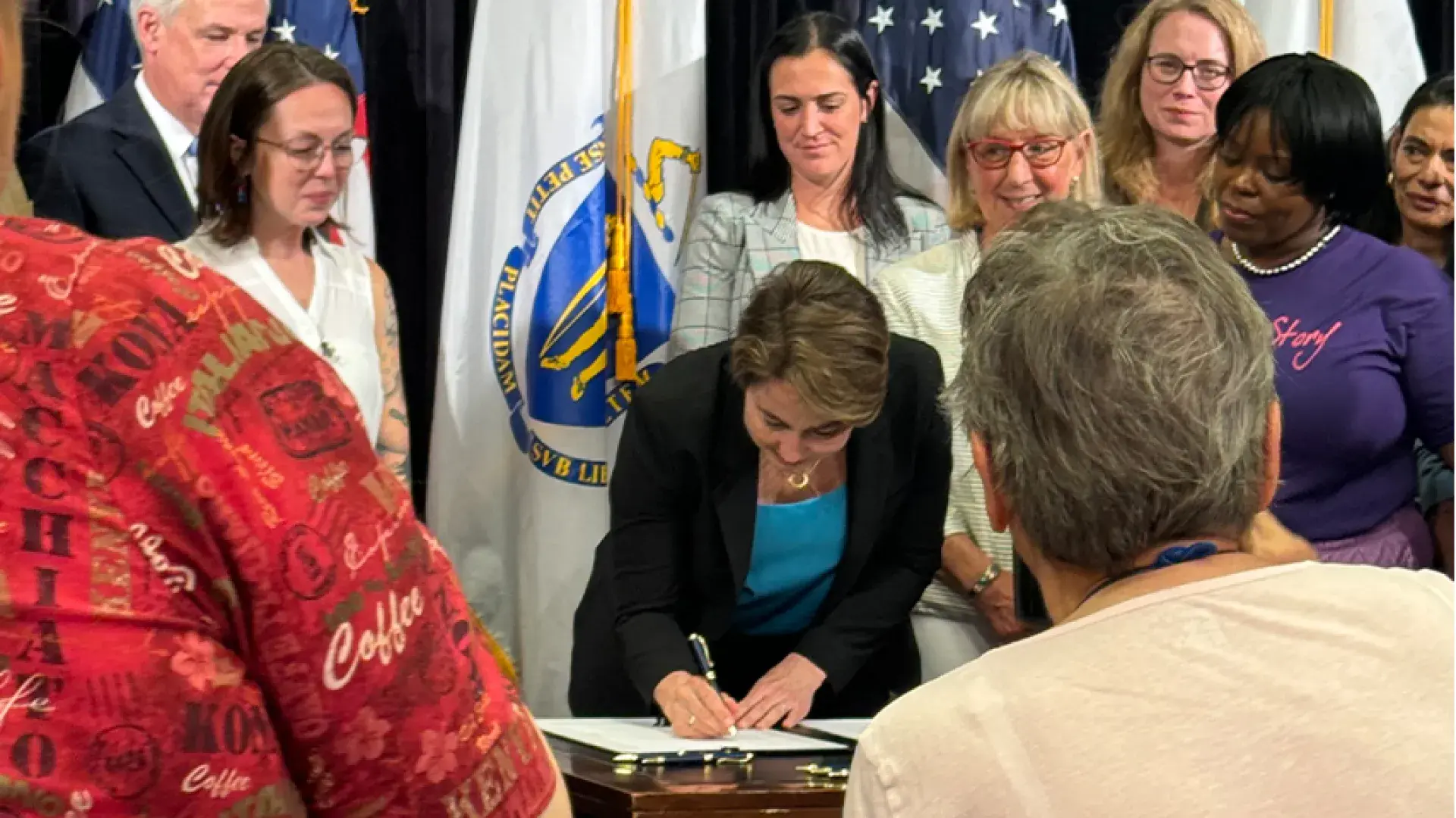 woman signs paper at desk with people all around