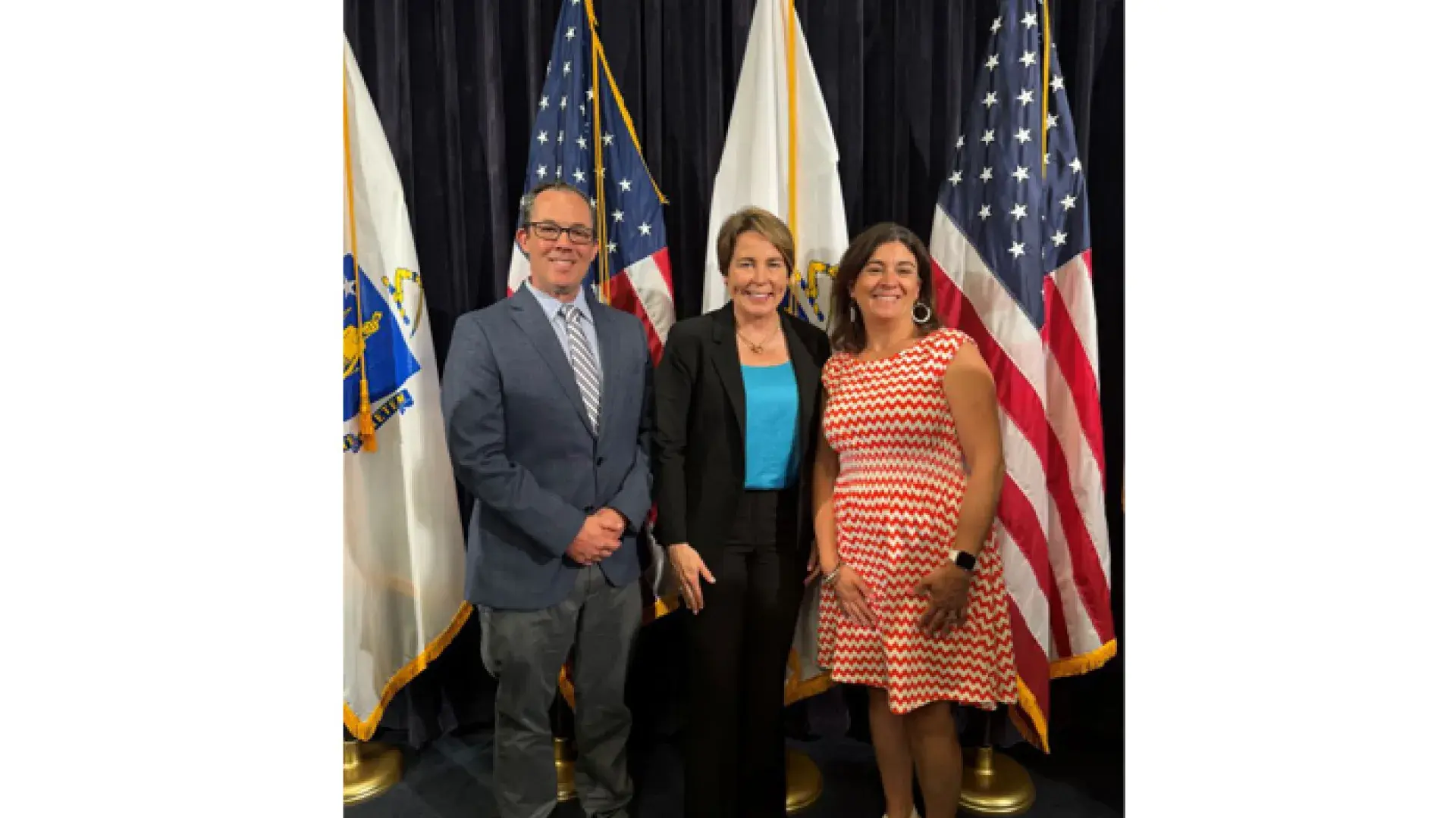 Three people stand in front of US and Massachusetts flags