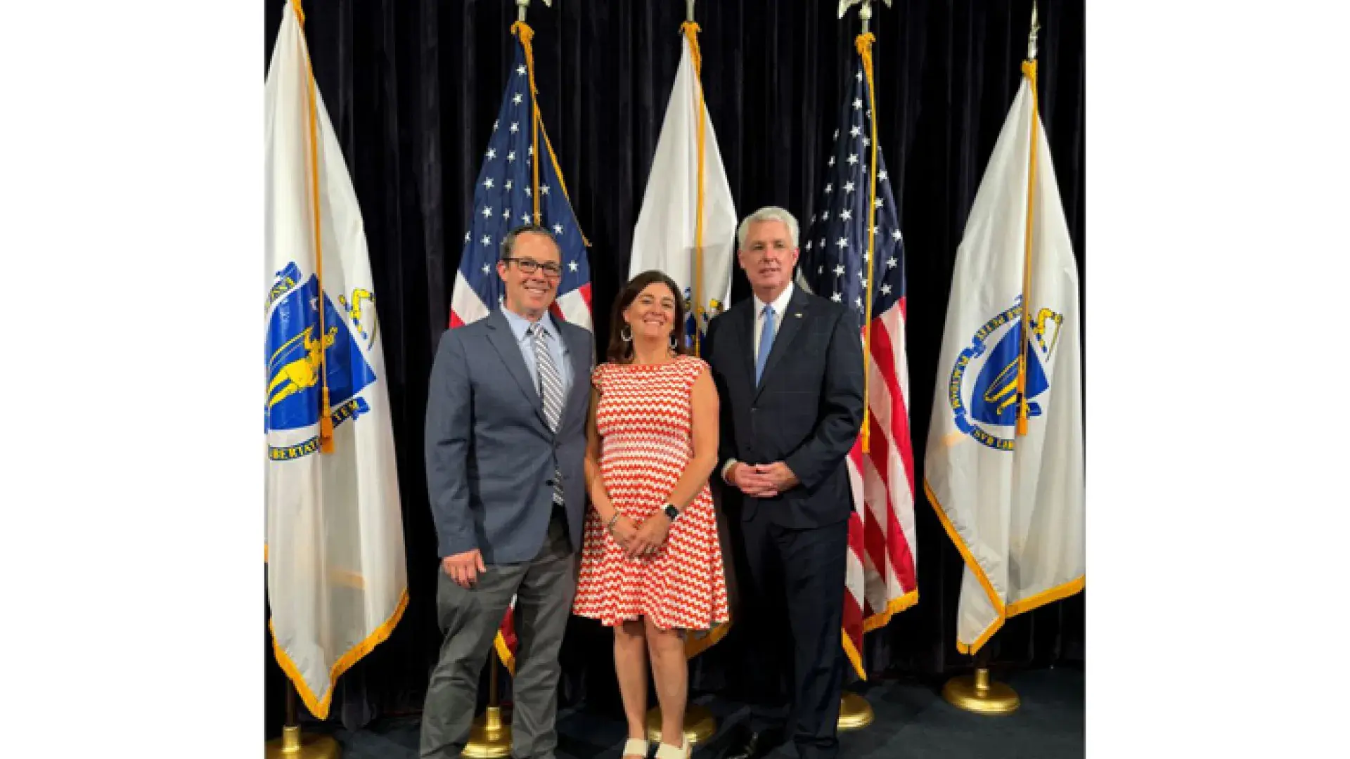 Three people stand in front of US and Massachusetts flags