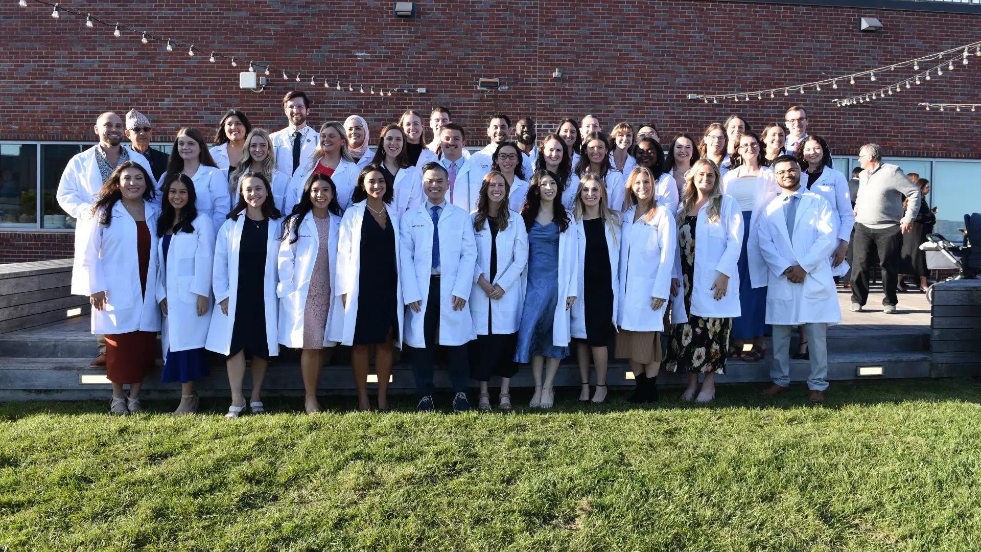A group of people wearing white medical coats stand in three lines for a photo