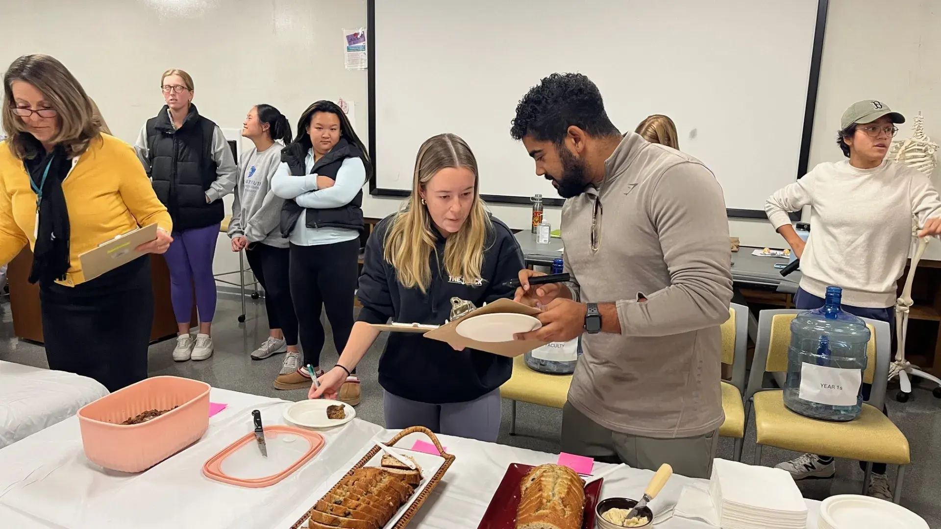 Two people stand in front of a table with loaves of bread while holding plates