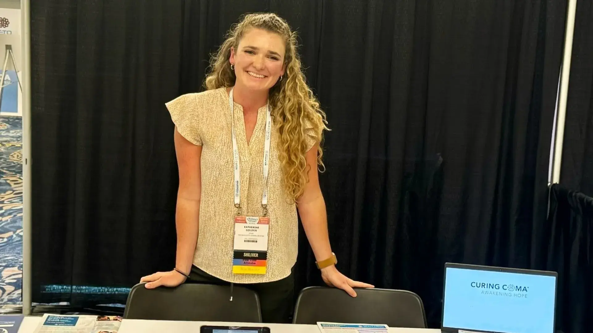 katie stands in front of a table full of papers at a conference
