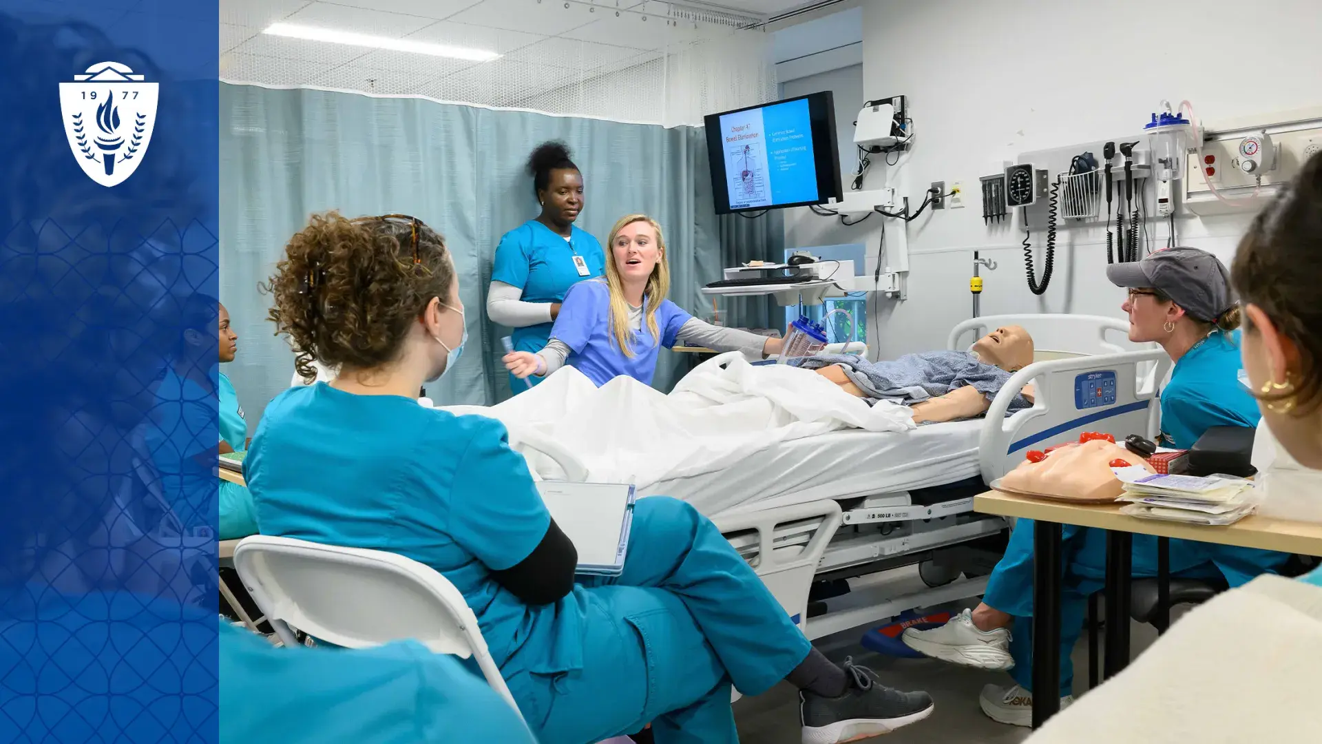 Simulation in healthcare education takes place with a manikin in a bed and nursing students in scrubs gathered around