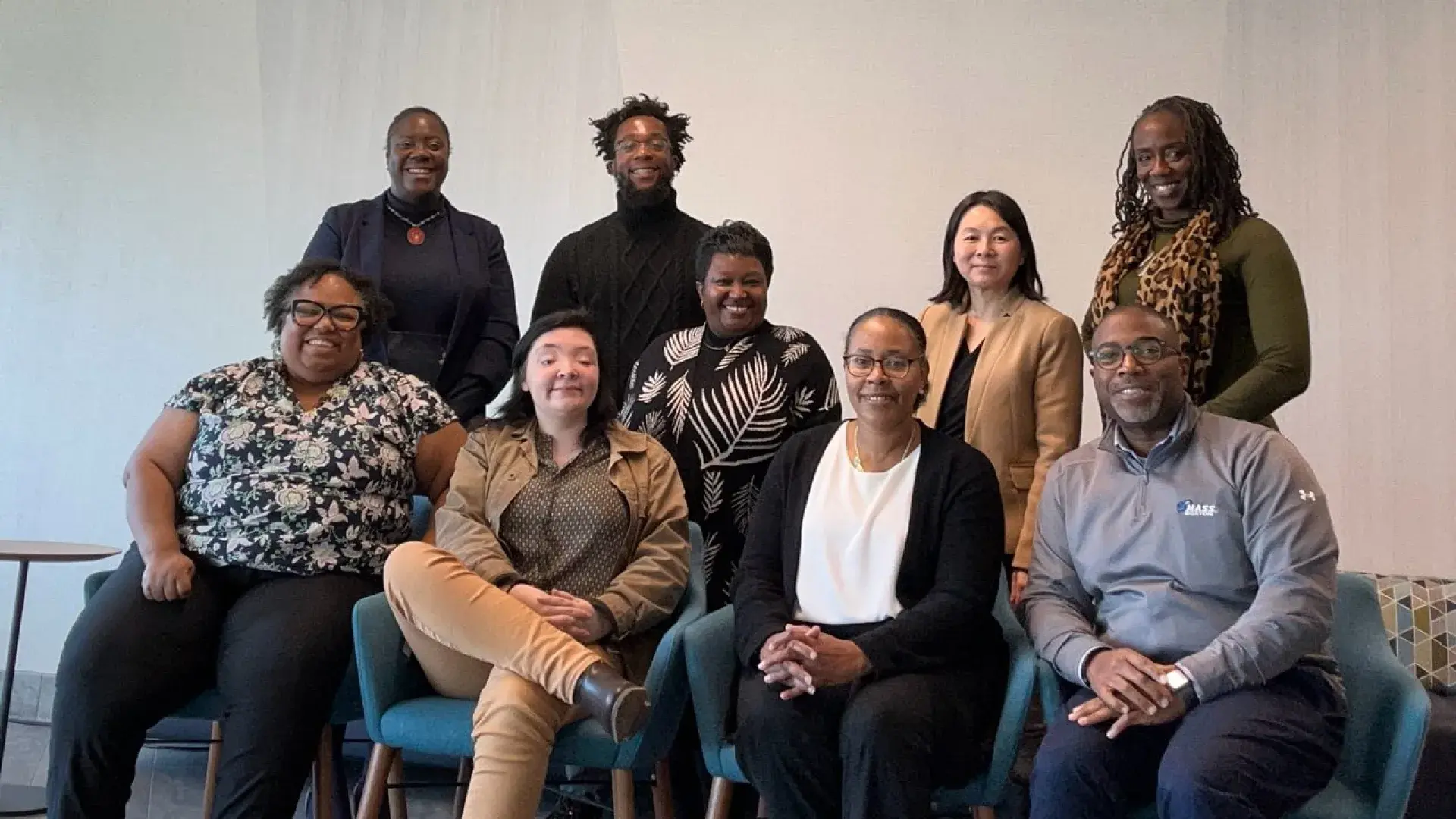 Four people sit in chairs while five people stand behind them