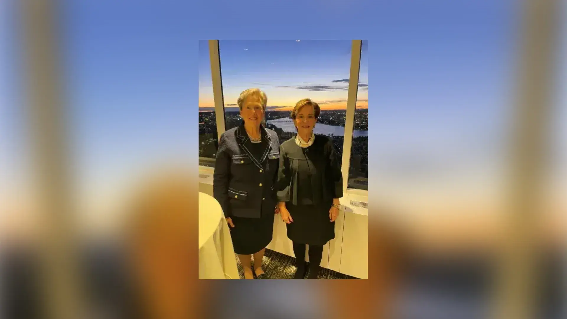 two women stand in front of a nighttime view out a window