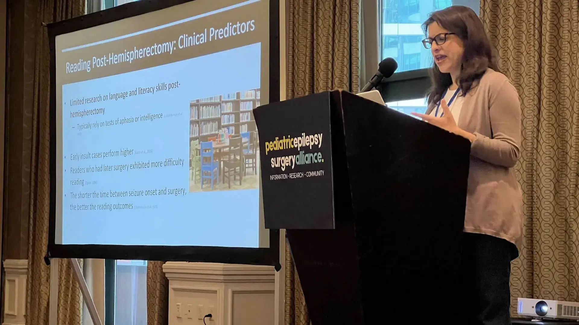 A woman stands behind a podium with a screen to her right
