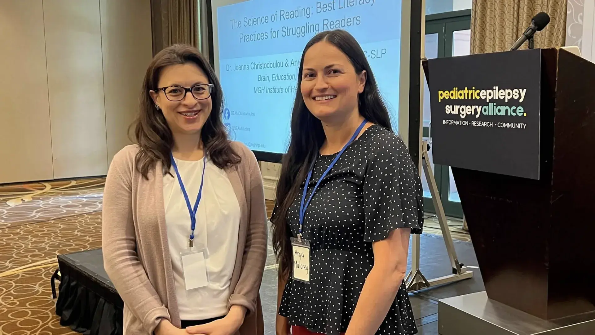 Two women stand in front of a podium with the words pediatric epilepsy surgery alliance