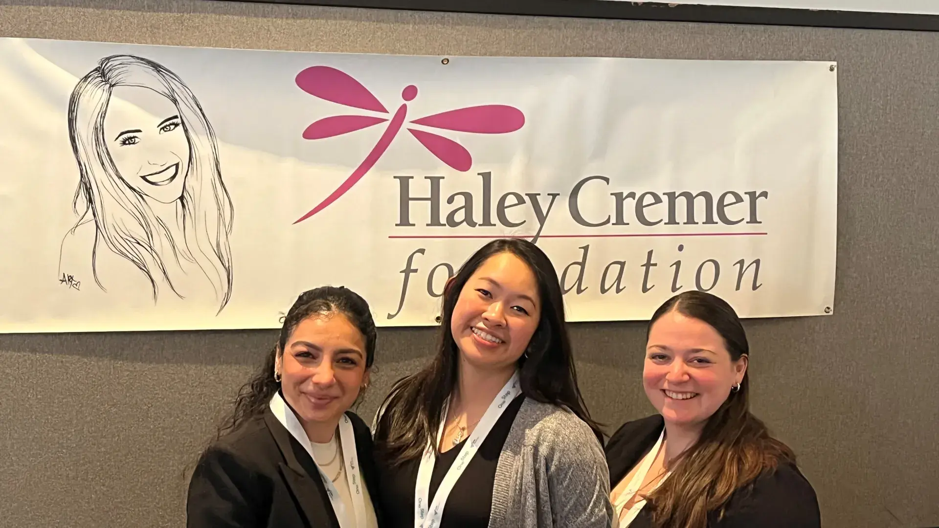 Three women stand in front of a sign with the words Haley Cremer Foundation