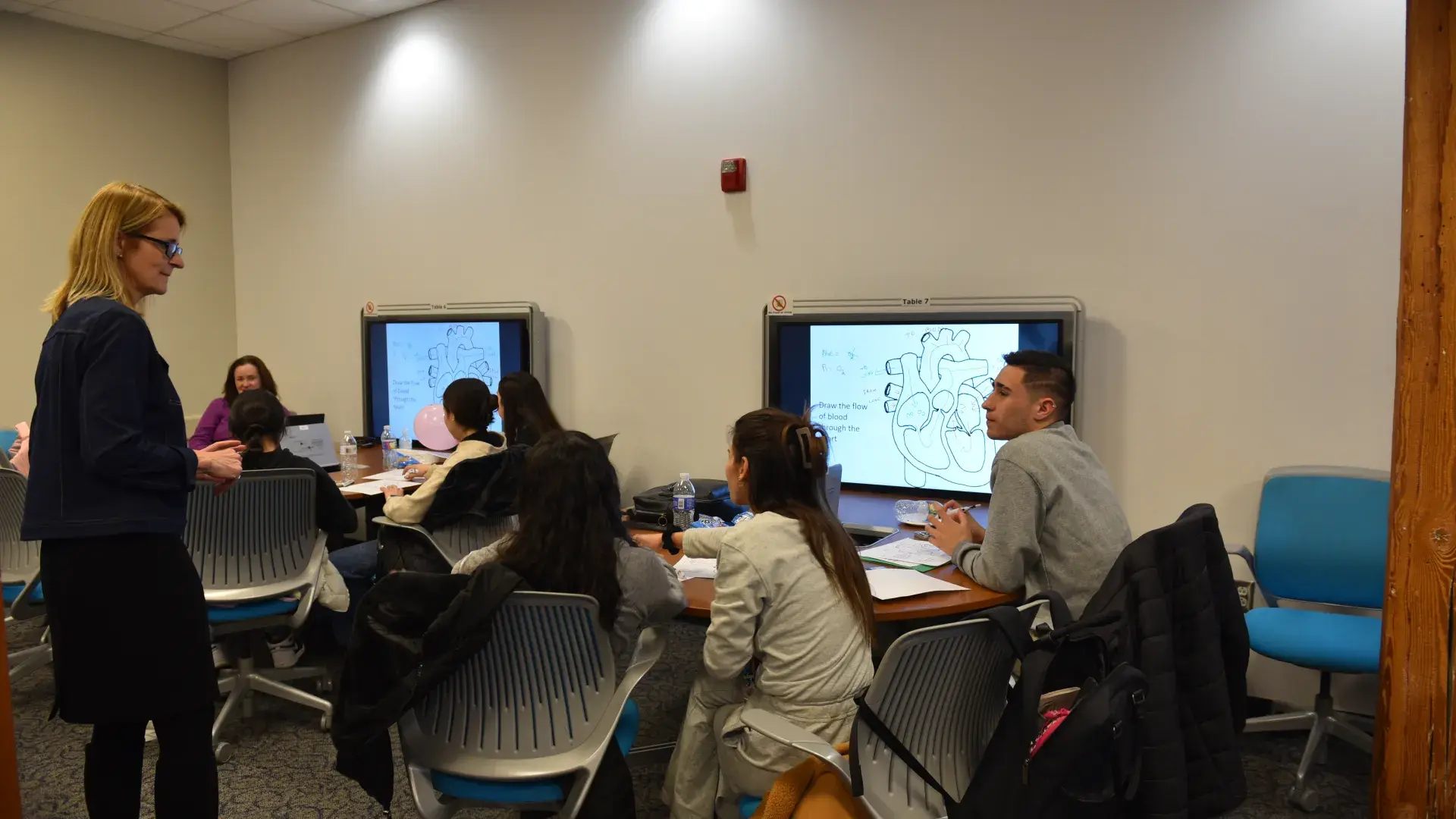 A woman who is standing faces a group of students sitting at a table