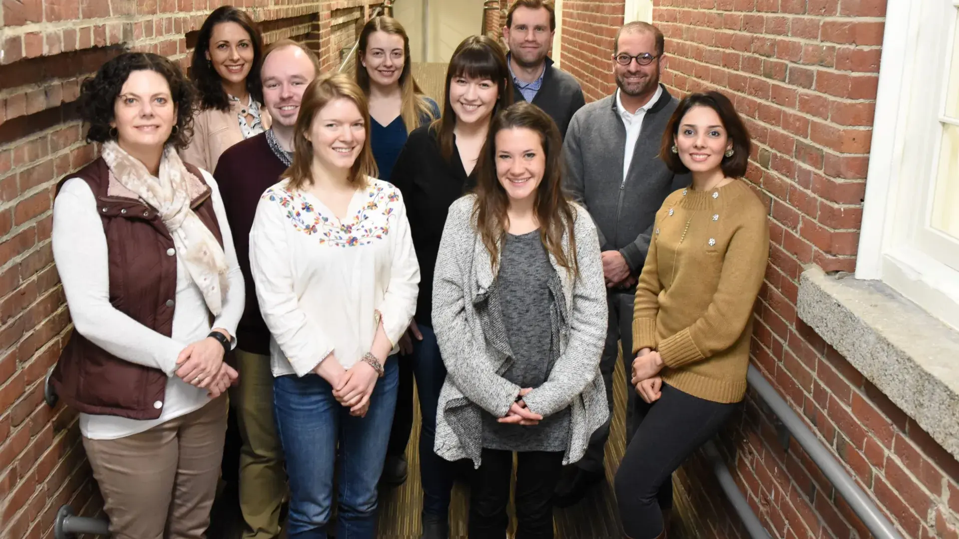 Ten people stand in a brick hallway posing for the camera