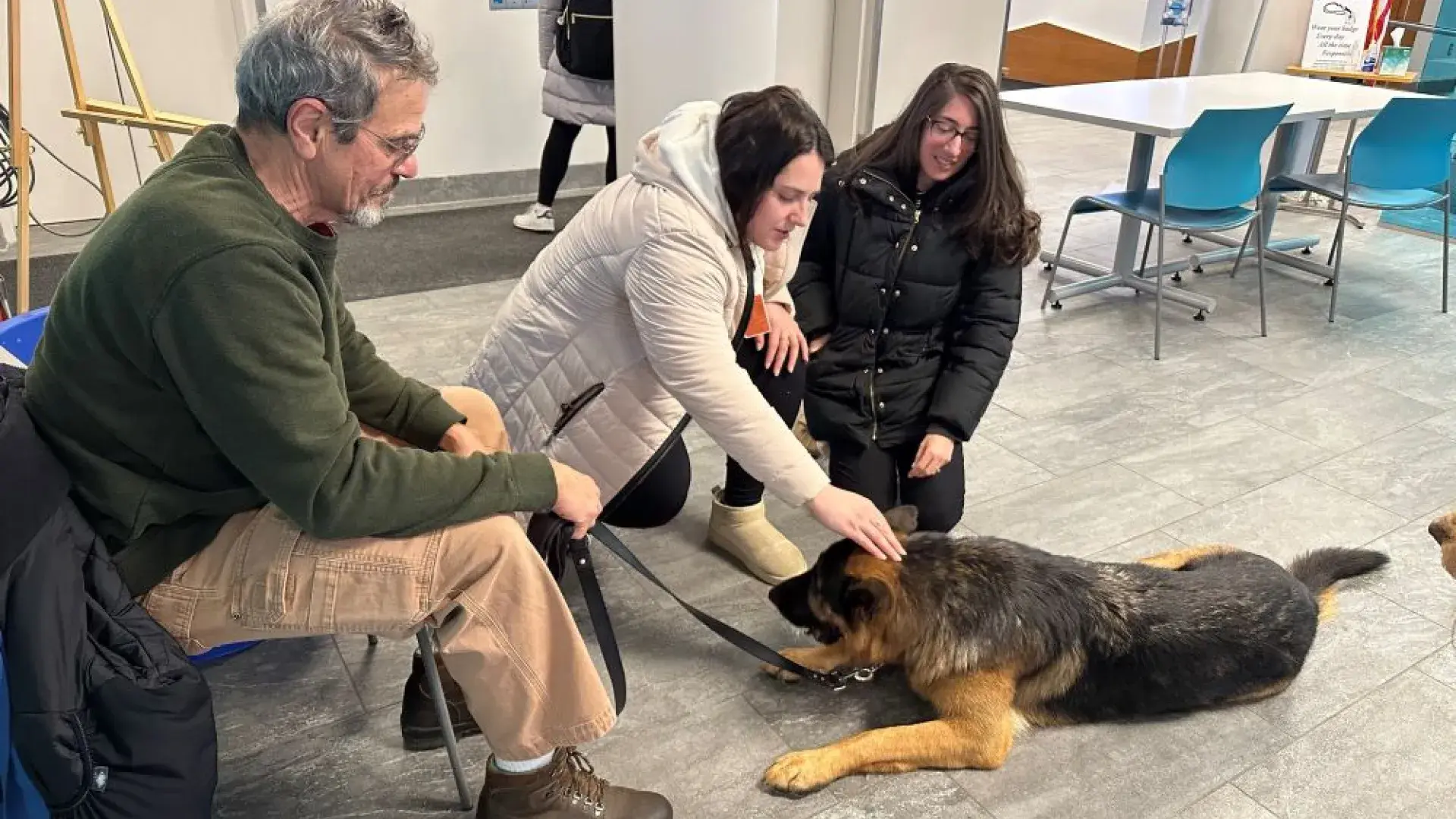 Two women pet a dog while a man site in a chair holding the leash