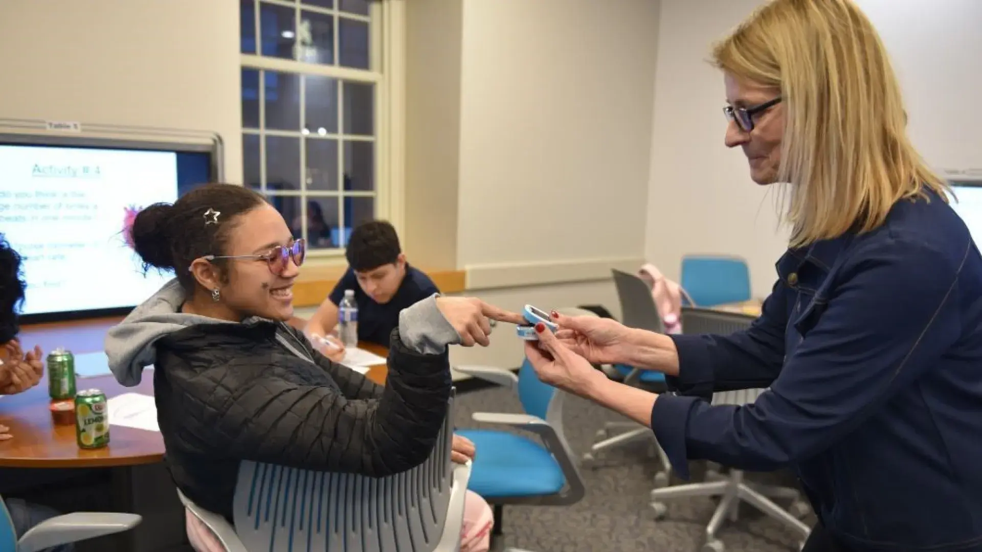 A woman places a device on the finger of a woman who is sitting down