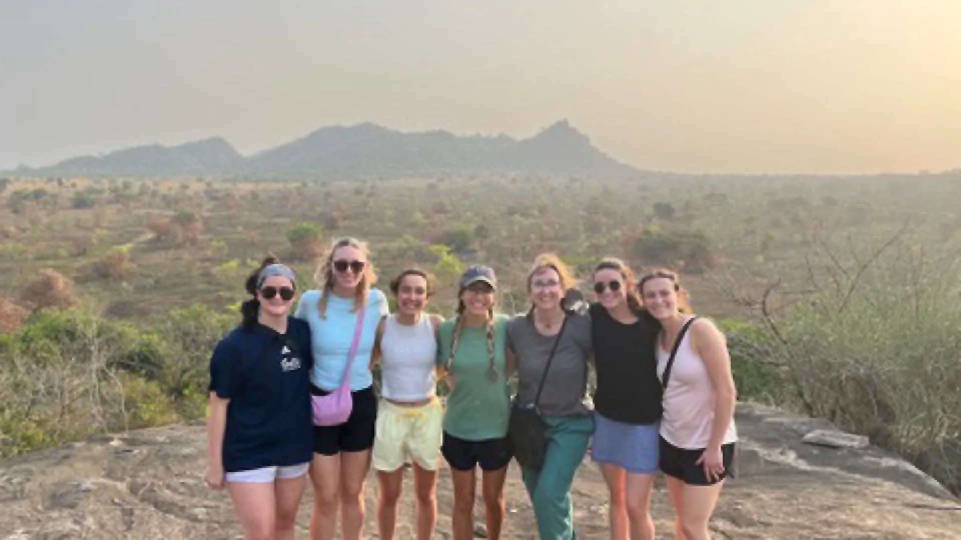 Seven women pose standing on a rock with mountains behind them