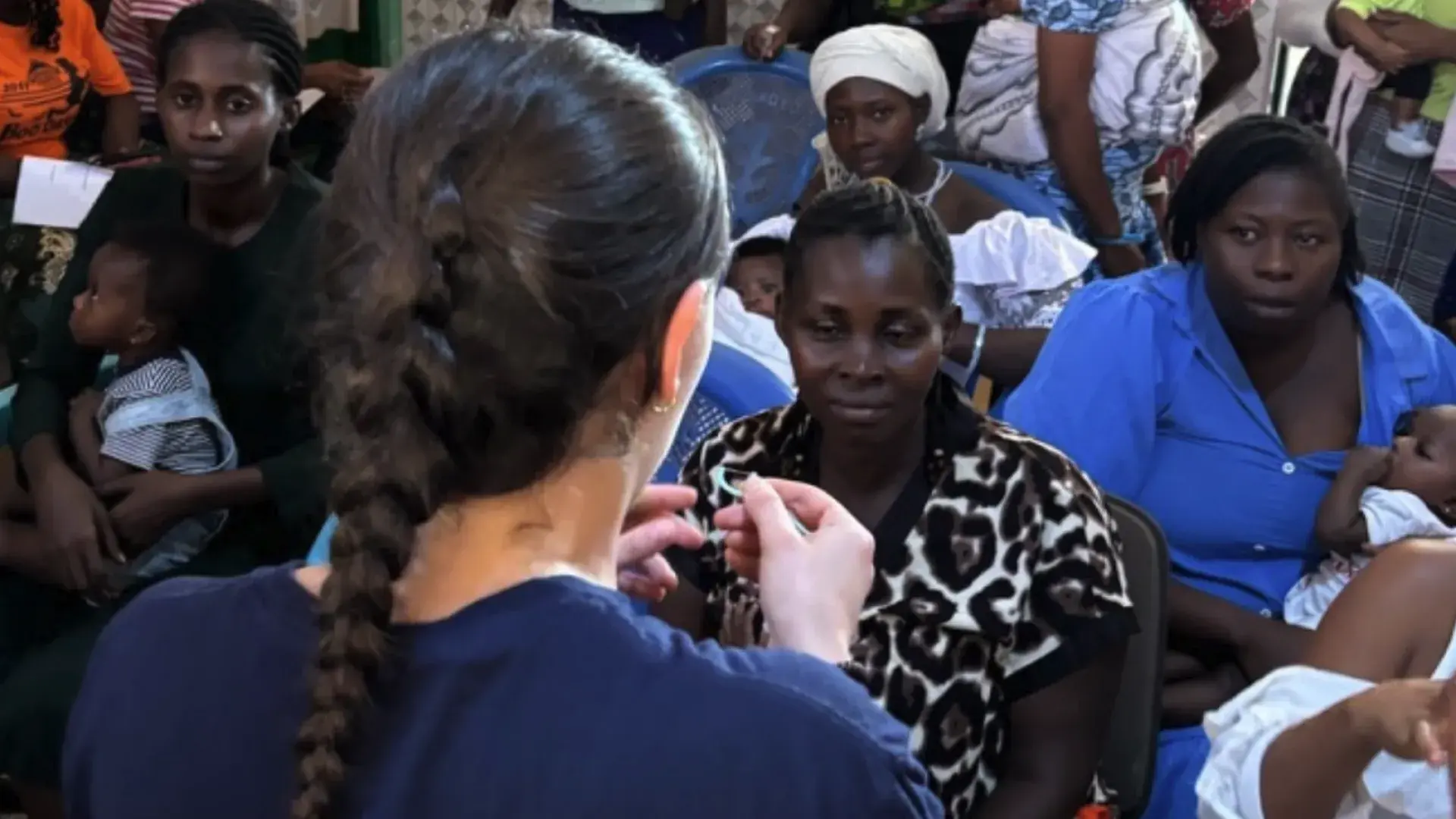 woman facing away from the camera stands in front of mothers and children